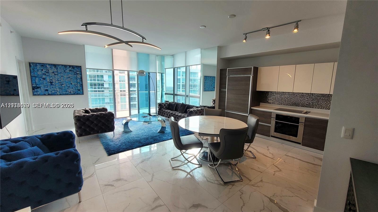 Open-concept living space featuring floor-to-ceiling windows, large-format tile flooring, modern kitchen cabinetry with built-in appliances, and desig