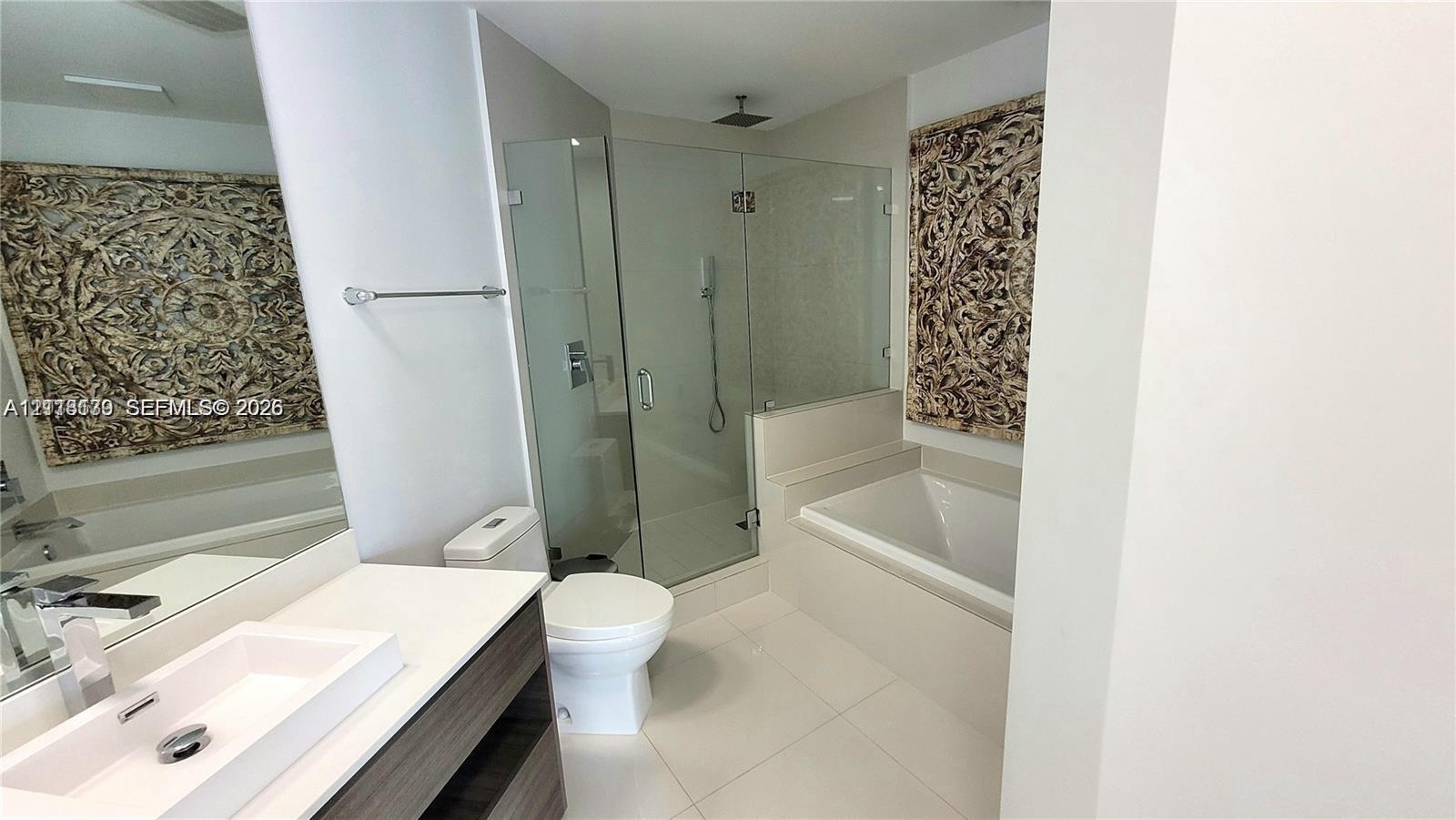 Bathroom featuring a rectangular vessel sink, floating vanity with wood-finish cabinetry, frameless glass-enclosed shower, soaking tub, and large wall