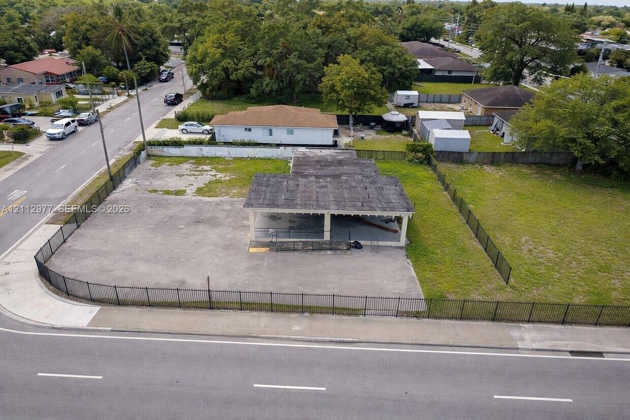 Expansive corner lot featuring a paved surface, structural covered area, and perimeter black metal fencing