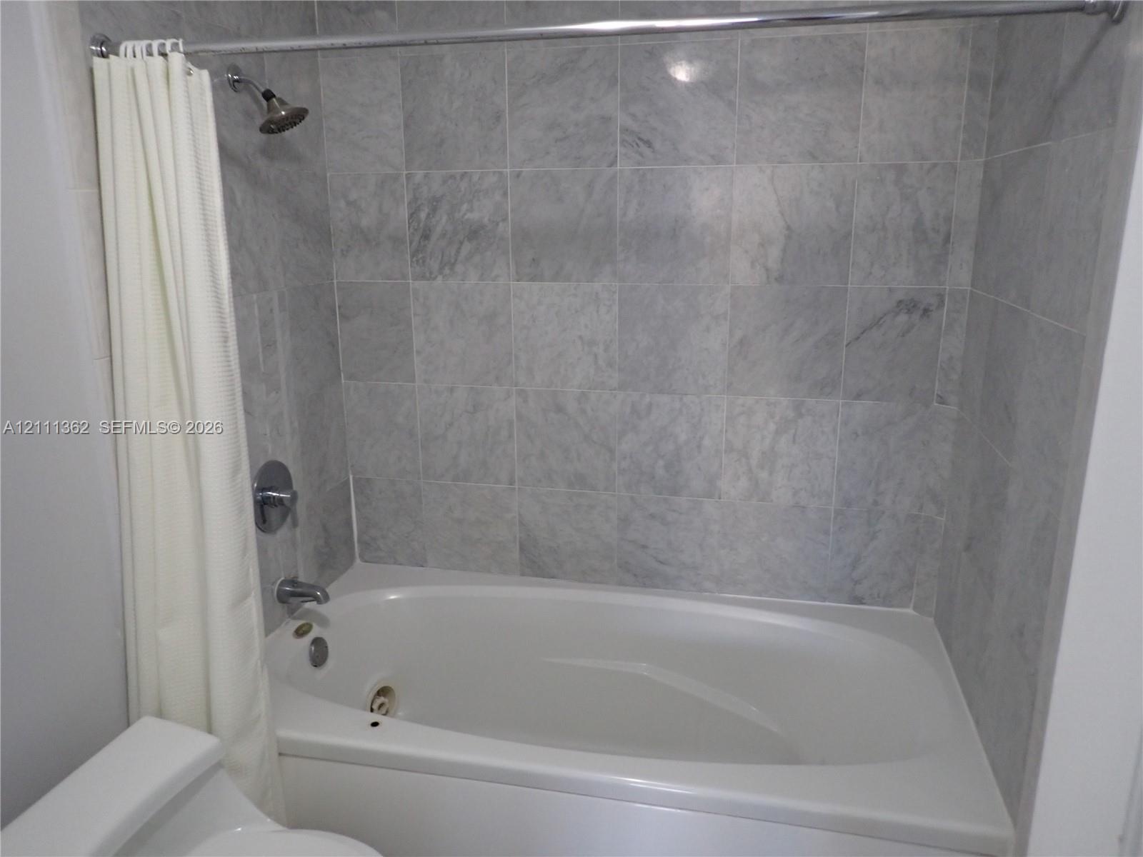 Full-size bathtub with integrated shower, stone tile wall surround, and polished chrome faucet fixtures