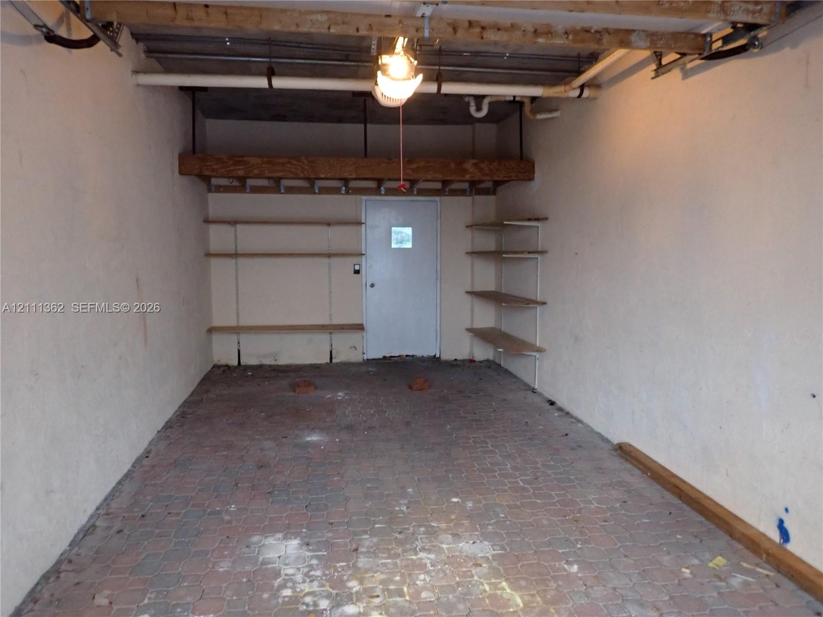 Enclosed garage featuring paved flooring, built-in wooden shelving units, and a dedicated overhead storage platform