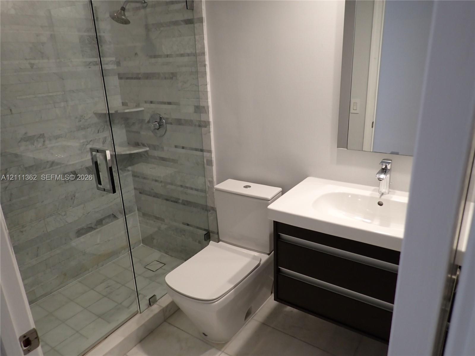 Bathroom featuring a floating vanity with a white countertop, an integrated sink with a chrome faucet, a glass-enclosed shower with horizontal wall ti
