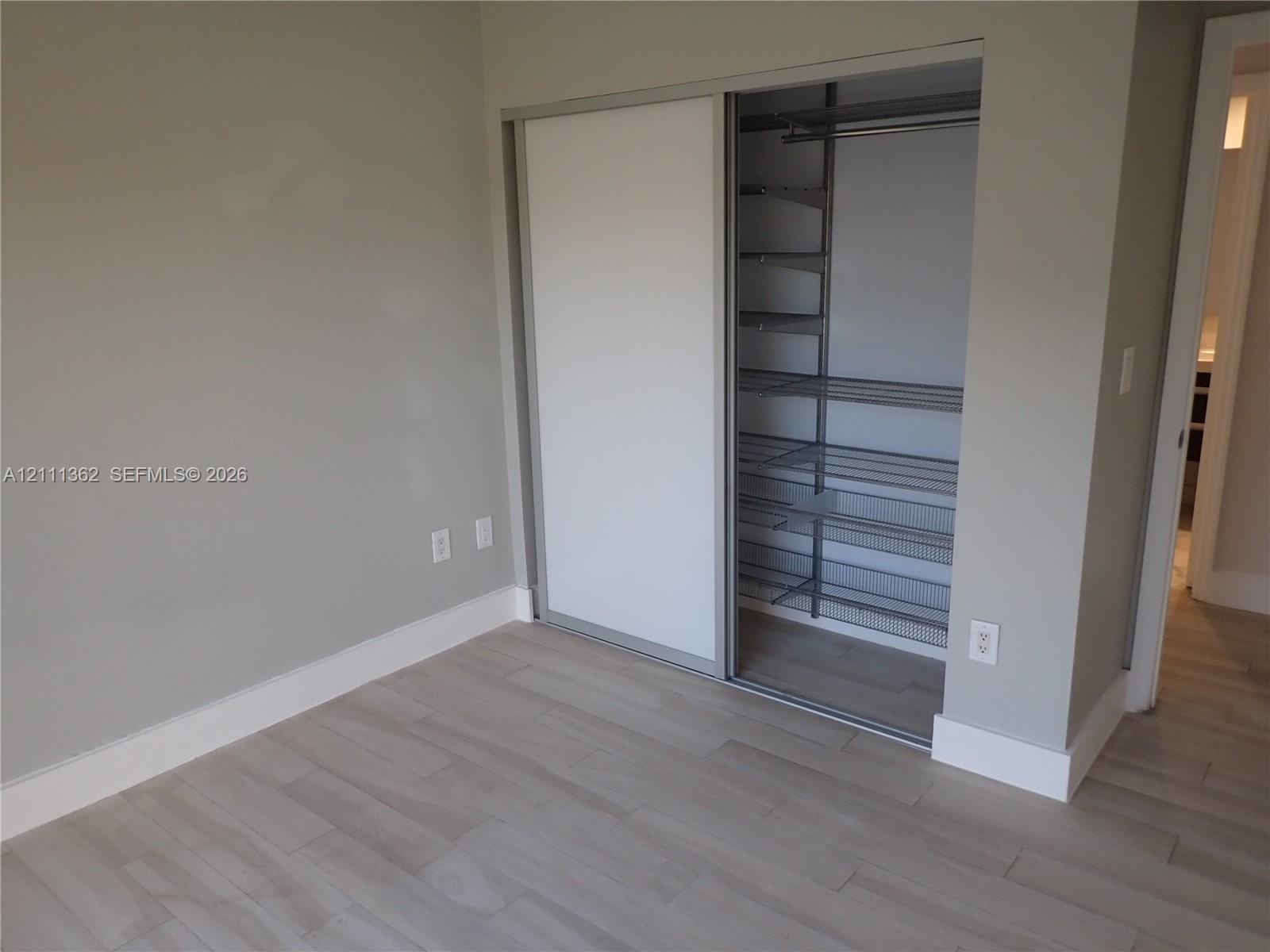 Closet with sliding doors and custom metal shelving, complemented by wood-finish flooring