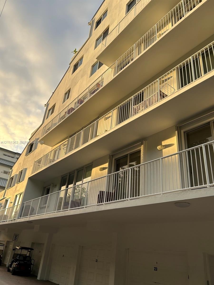 Multi-story building exterior featuring stacked private balconies with white railings, sliding glass doors, and ground-level garage access