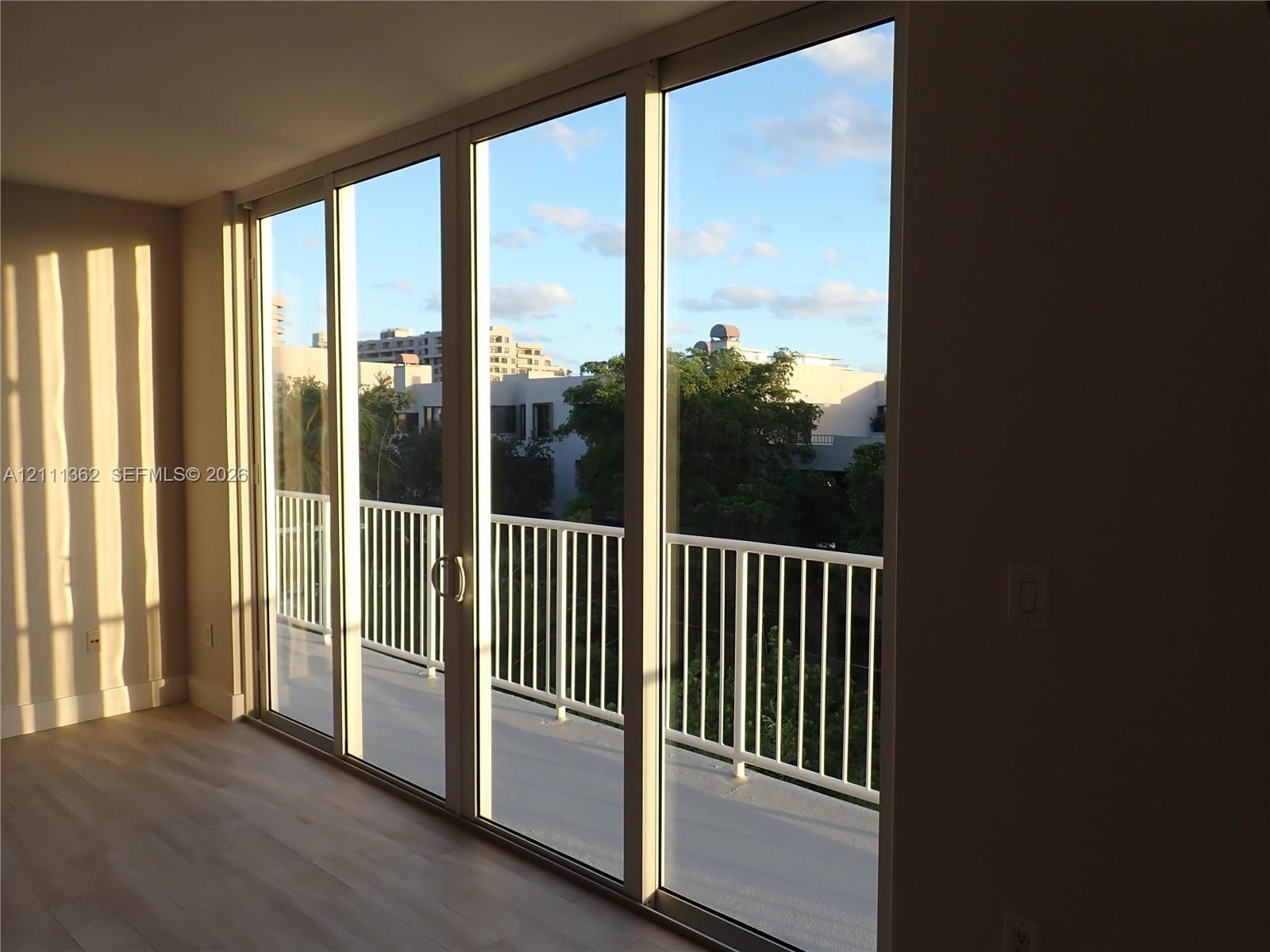 Floor-to-ceiling sliding glass panels, balcony with white metal railing, and wood-finish flooring