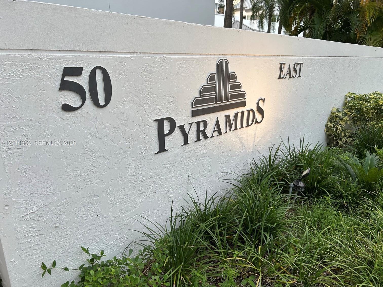 Stucco masonry monument sign featuring dimensional metal lettering and integrated low-voltage ground lighting, accented by foundational lush tropical 