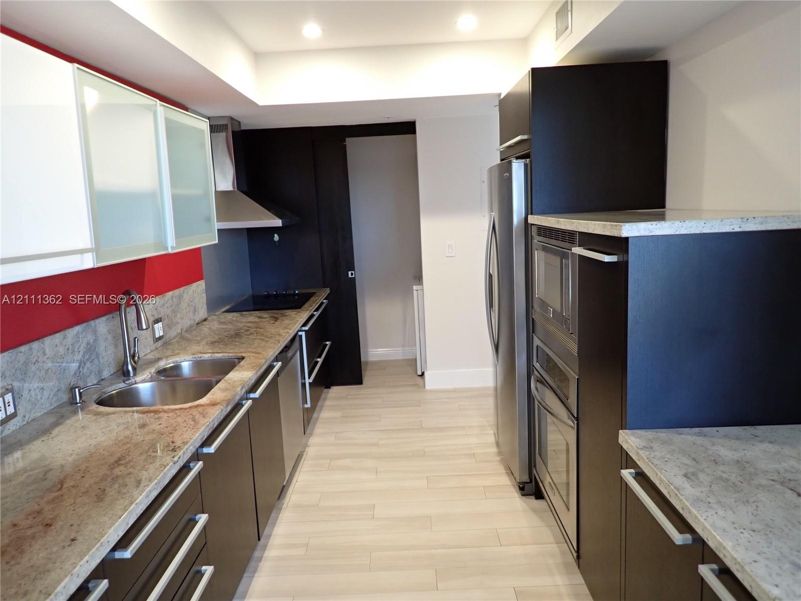 Kitchen featuring dark cabinetry, stone countertops, stainless steel appliances, recessed ceiling lighting, and wood-finish tile flooring
