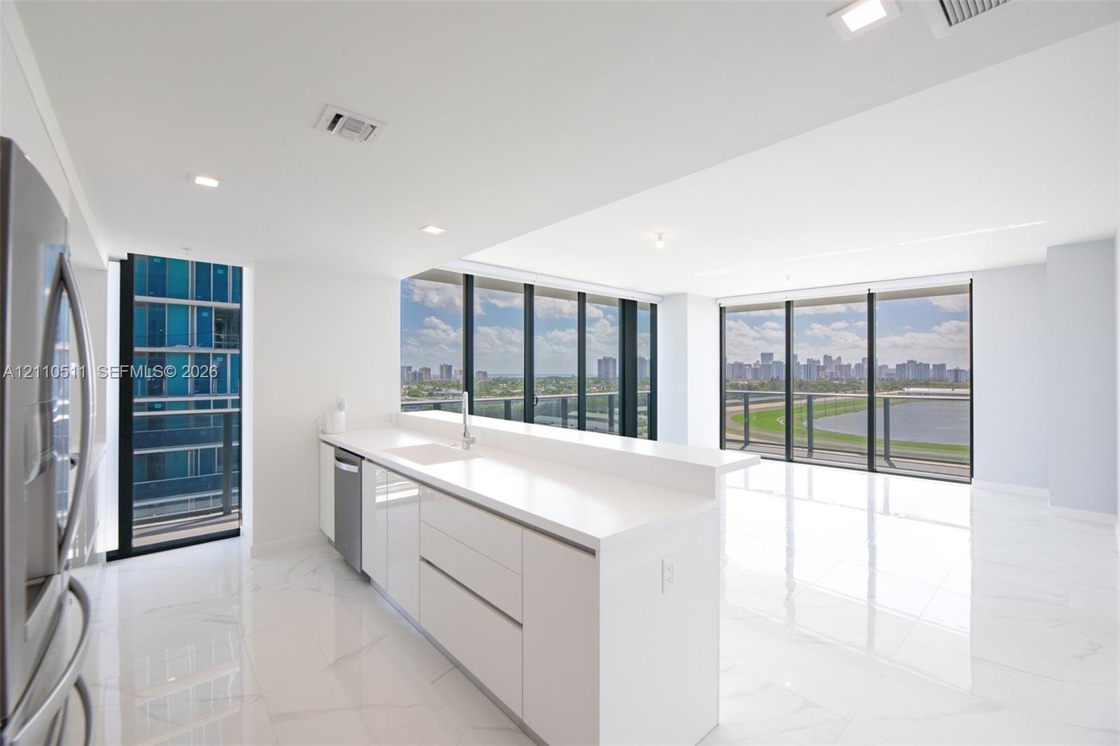Modern kitchen featuring white flat-panel cabinetry, quartz countertops, a stainless steel dishwasher, stone-finish tile flooring, and floor-to-ceilin