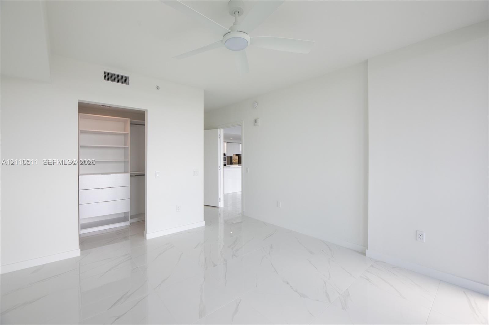 Interior space featuring white stone-finish tile flooring, ceiling fan with integrated lighting, and walk-in closet with built-in shelving and drawer 