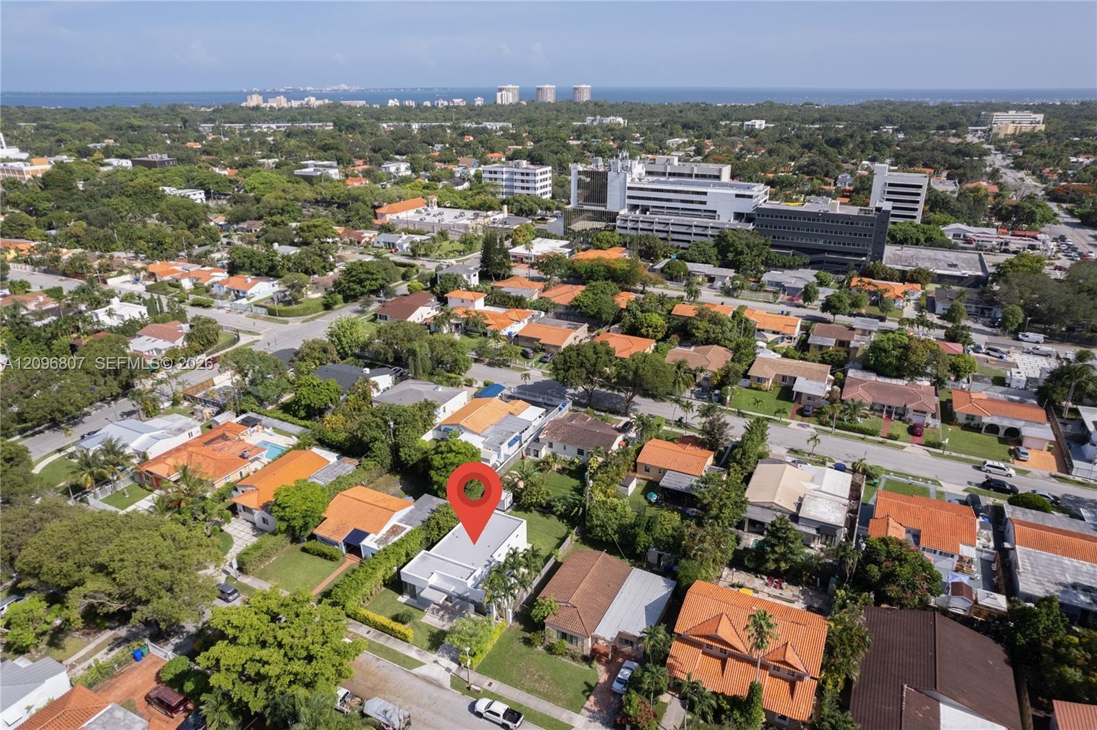 Aerial perspective featuring a flat-roof residence situated on a landscaped lot with mature palm trees and established perimeter vegetation