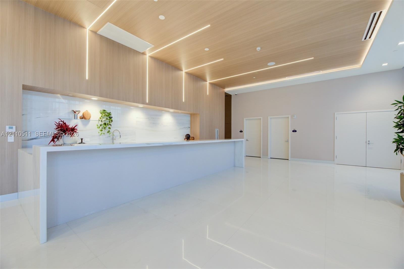 Large kitchen island with a white waterfall countertop, expansive wood-paneled wall with integrated linear lighting, stone-tiled backsplash, polished 