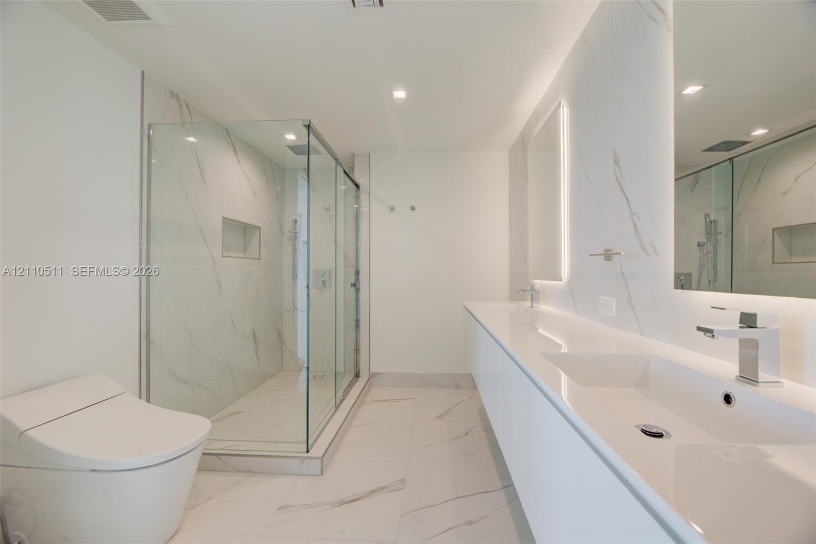 Bathroom featuring a dual-sink vanity with a solid-surface countertop, walk-in glass-enclosed shower with wall-mounted plumbing fixtures, recessed sho
