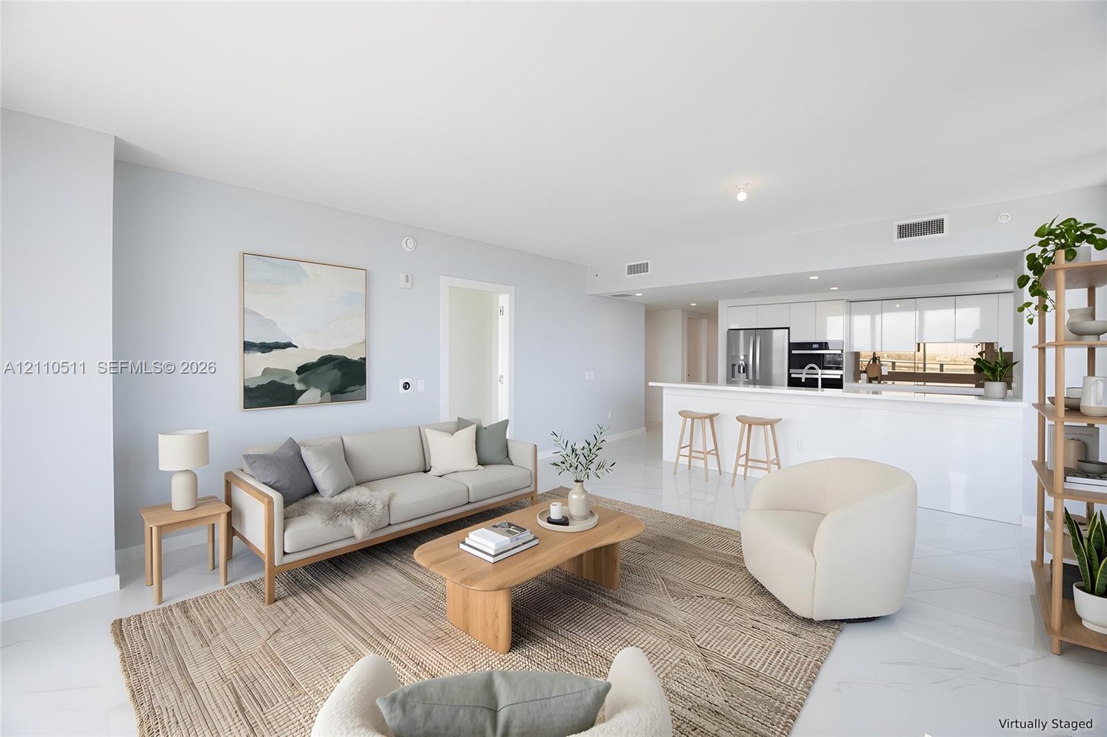Open-concept living space featuring high-gloss tile flooring, white cabinetry, integrated stainless steel appliances, and a peninsula with solid-surfa