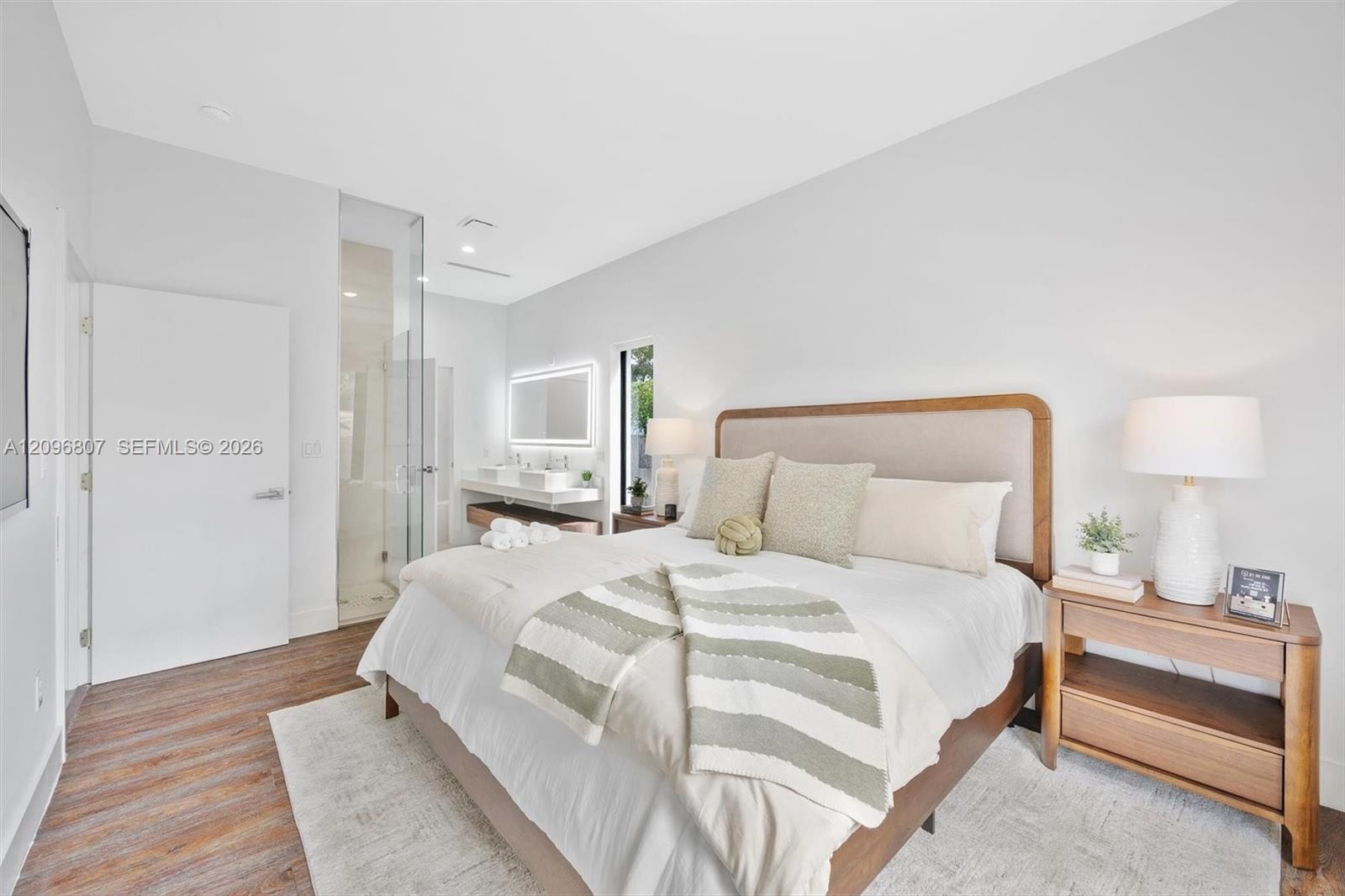 Wood-finish flooring, glass-enclosed shower, wall-mounted double vanity, and back-lit rectangular mirror