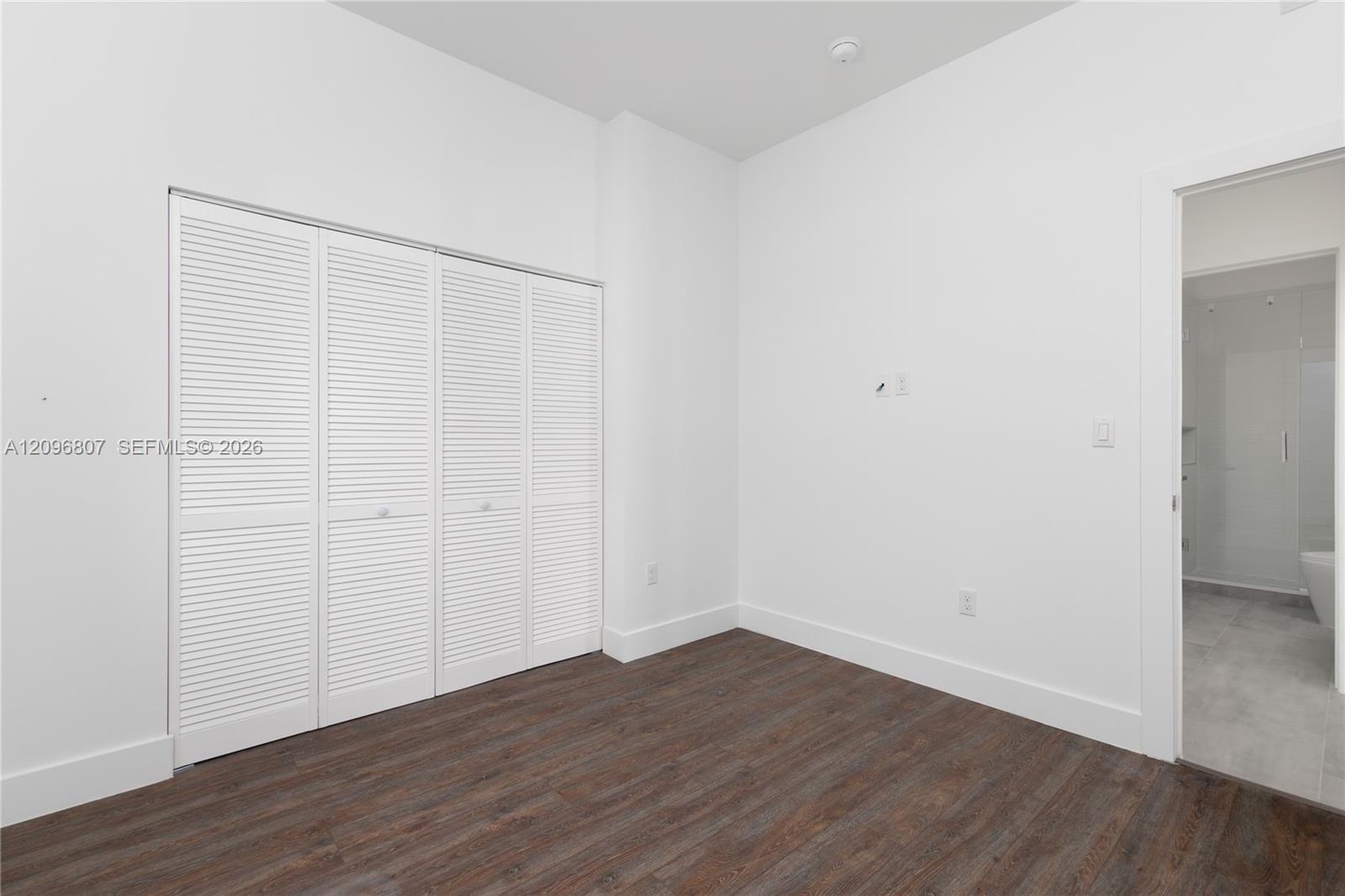 Room featuring wood-finish flooring, white walls, and a four-panel louvered closet door