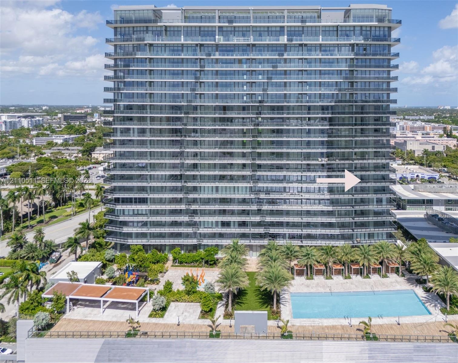 High-rise architectural exterior featuring glass-paneled balconies, a ground-level swimming pool, hardscaped patio, integrated landscaping, and covere