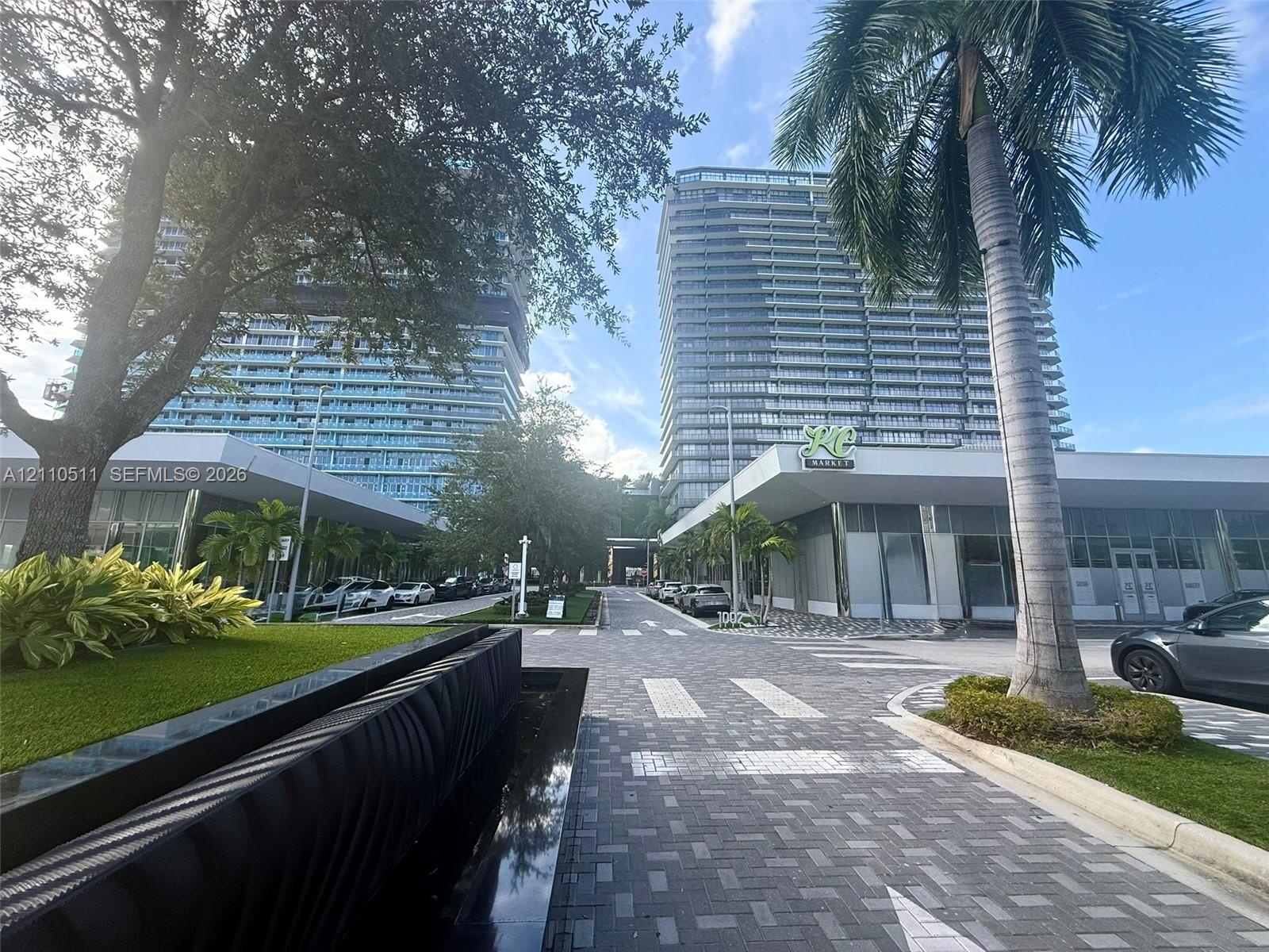 High-rise architectural exterior featuring glass curtain walls, multi-level structural design, stone-paver pedestrian walkways, decorative water featu