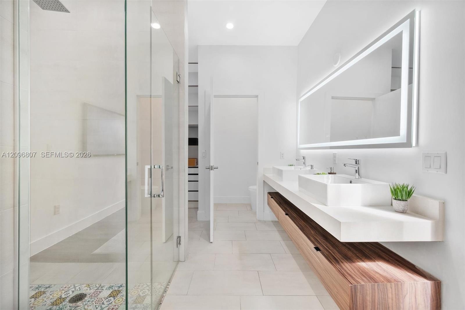 Floating dual-sink vanity with wood-finish cabinetry, quartz countertops, frameless glass walk-in shower with decorative tile accents, and an integrat