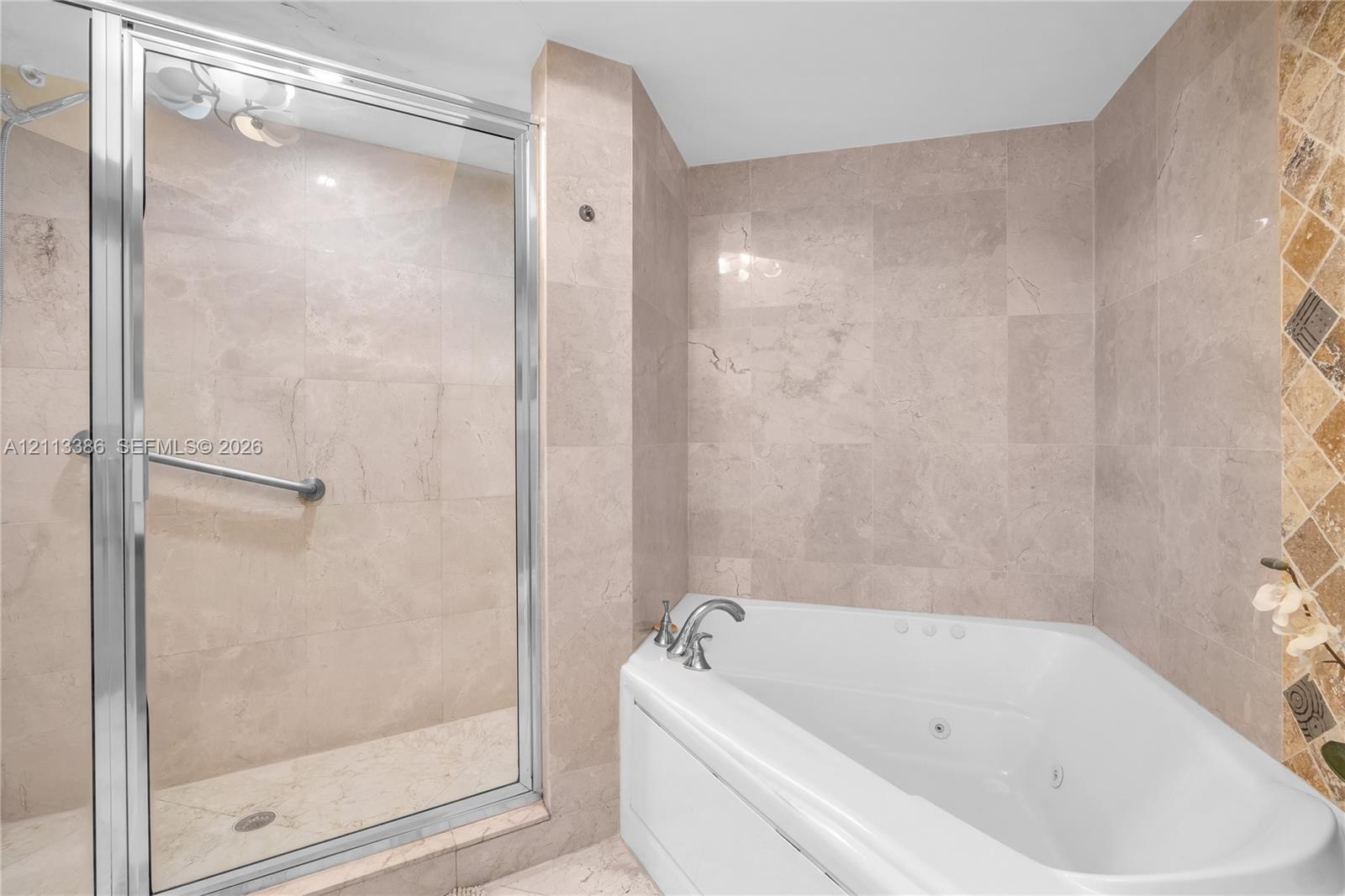 Glass-enclosed shower with metal grab bar, jetted corner tub, and neutral stone tile surround