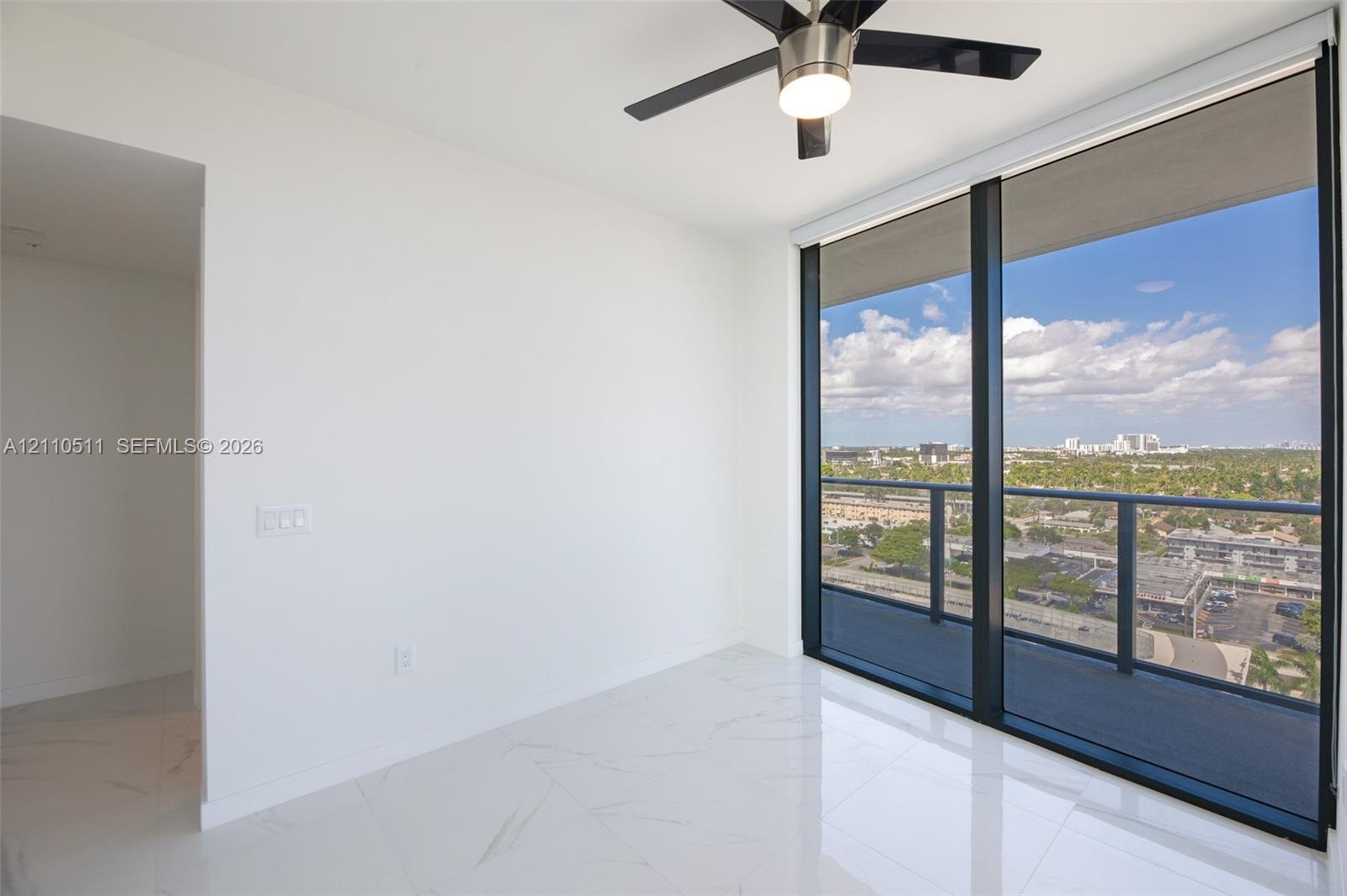 Second bedroom, floor-to-ceiling windows, high-gloss stone-finish flooring, private balcony with metal railing, and integrated ceiling fan with lighti