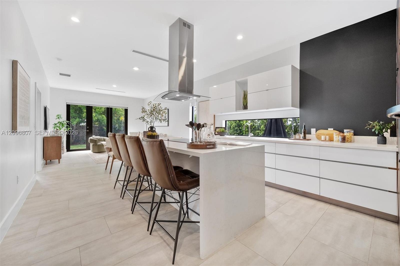 Kitchen featuring a large central island with quartz countertops, minimalist high-gloss white cabinetry, a stainless steel chimney-style range hood, a