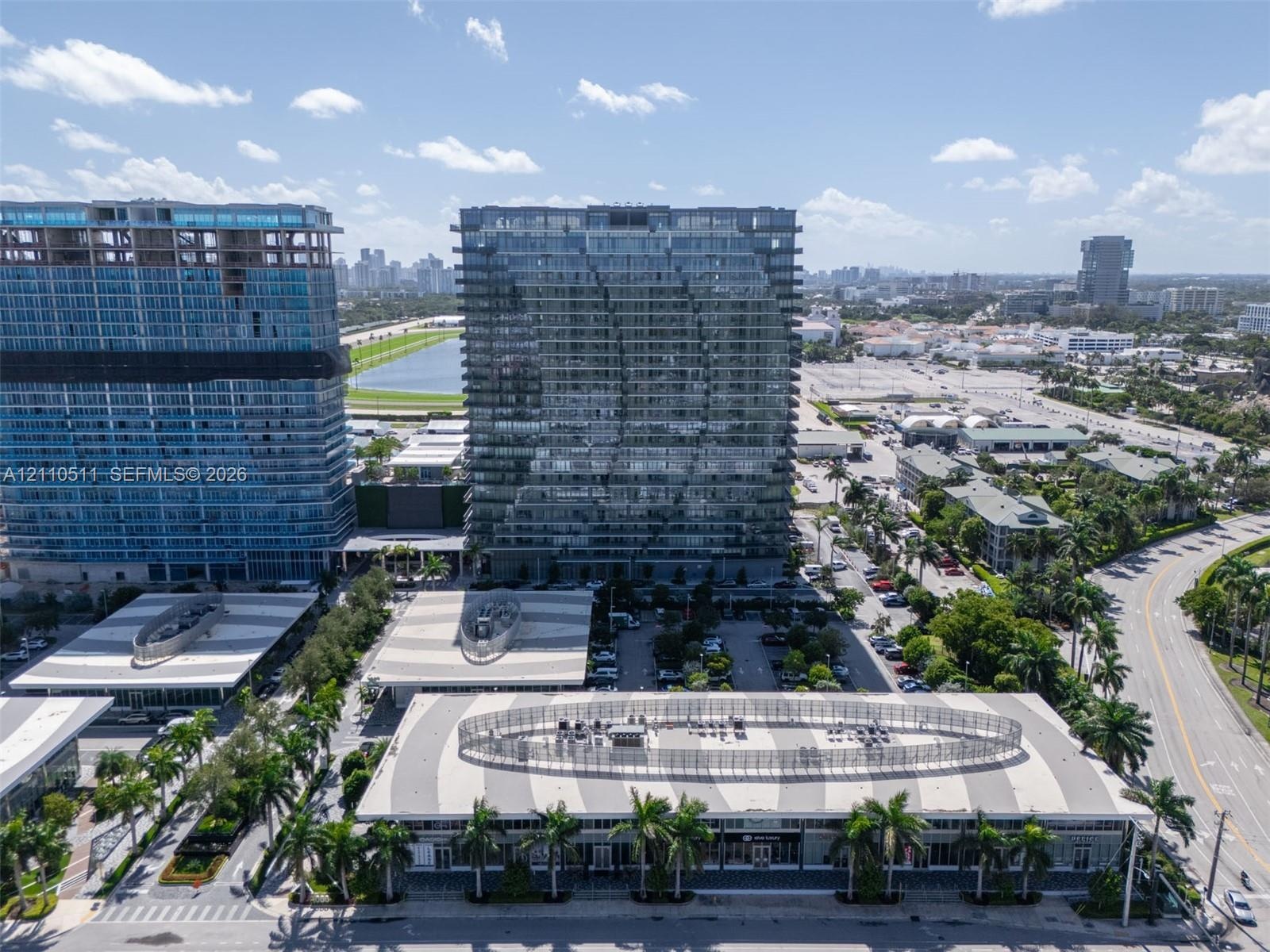 Aerial perspective of high-rise glass-facade towers featuring structured parking facilities with geometric roof patterns and integrated palm tree land