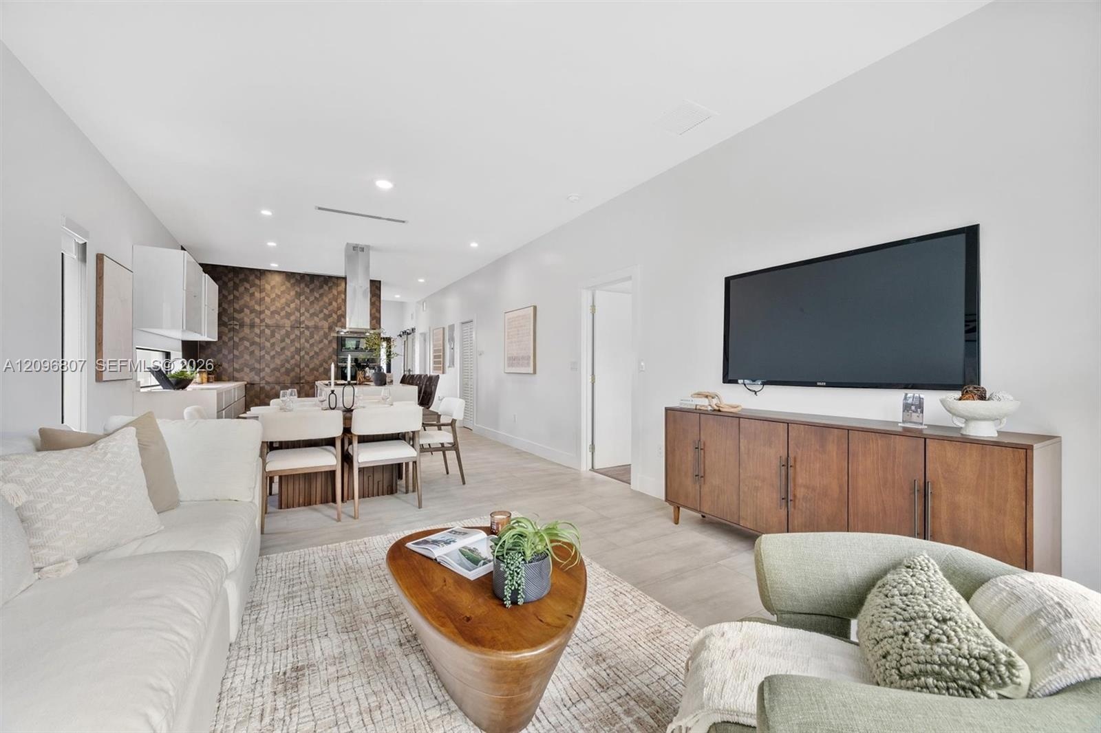 Open-concept interior featuring light wood-finish flooring, recessed lighting, and a textured geometric accent wall in the kitchen