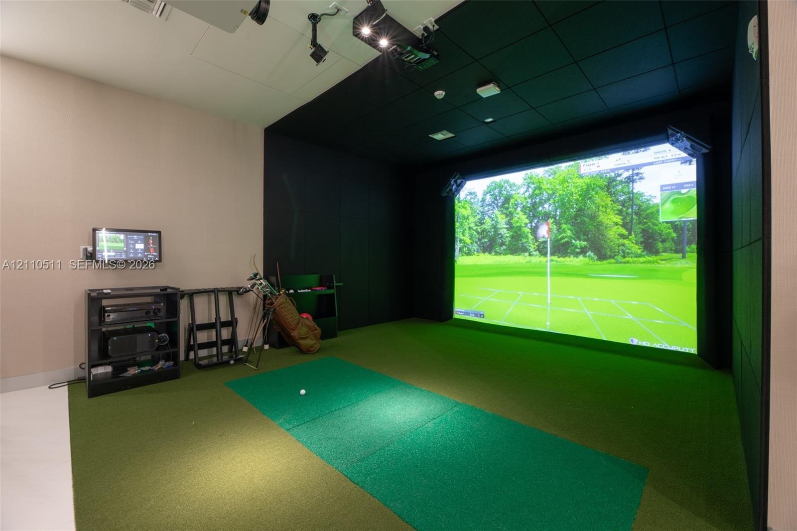 Golf simulator room featuring a large-scale projection screen, synthetic turf flooring, sound-dampening wall panels, and ceiling-mounted projection ha