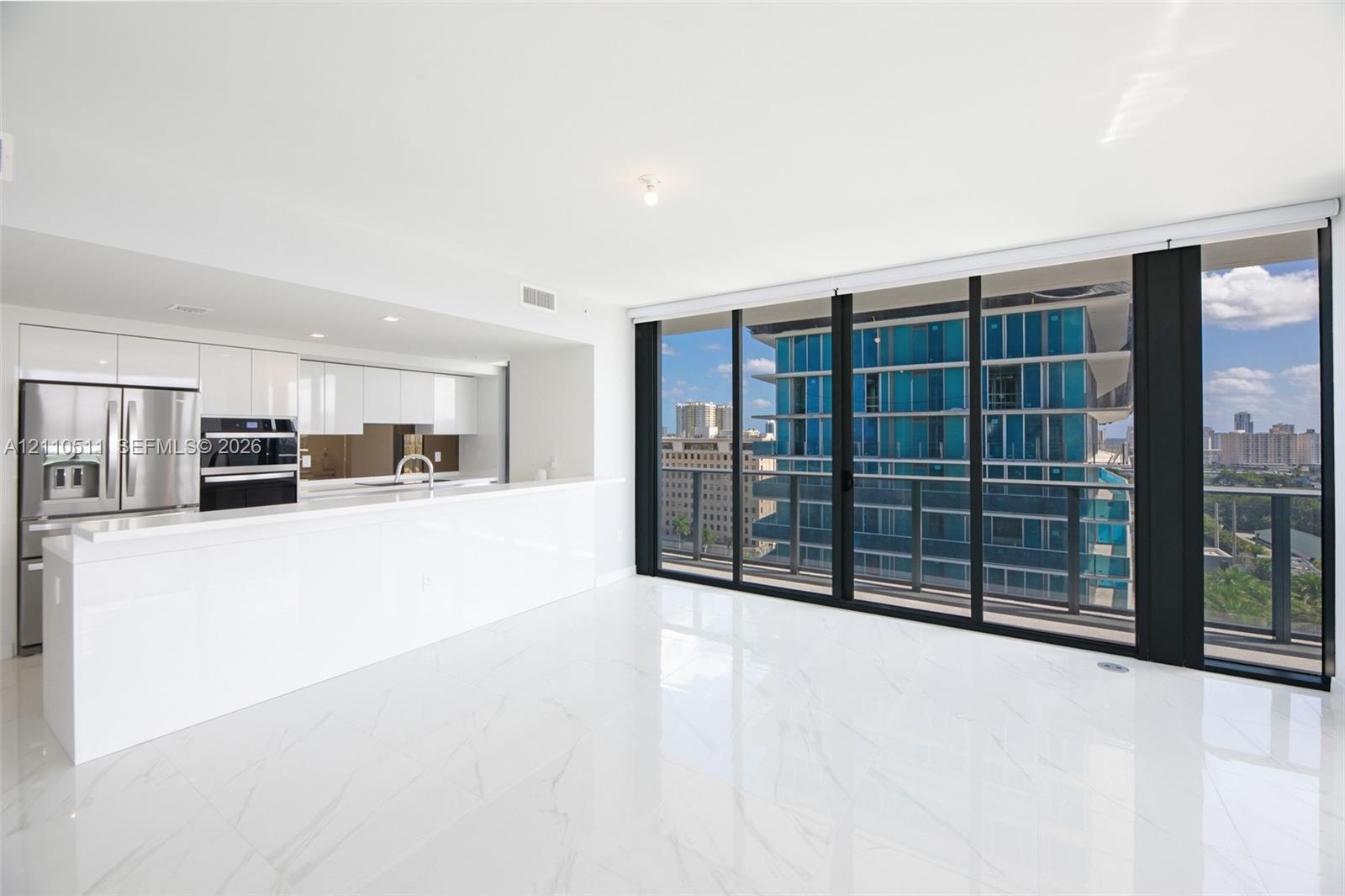 Open-concept kitchen featuring high-gloss cabinetry, stainless steel appliances, and a breakfast bar, highlighted by large-format flooring and floor-t