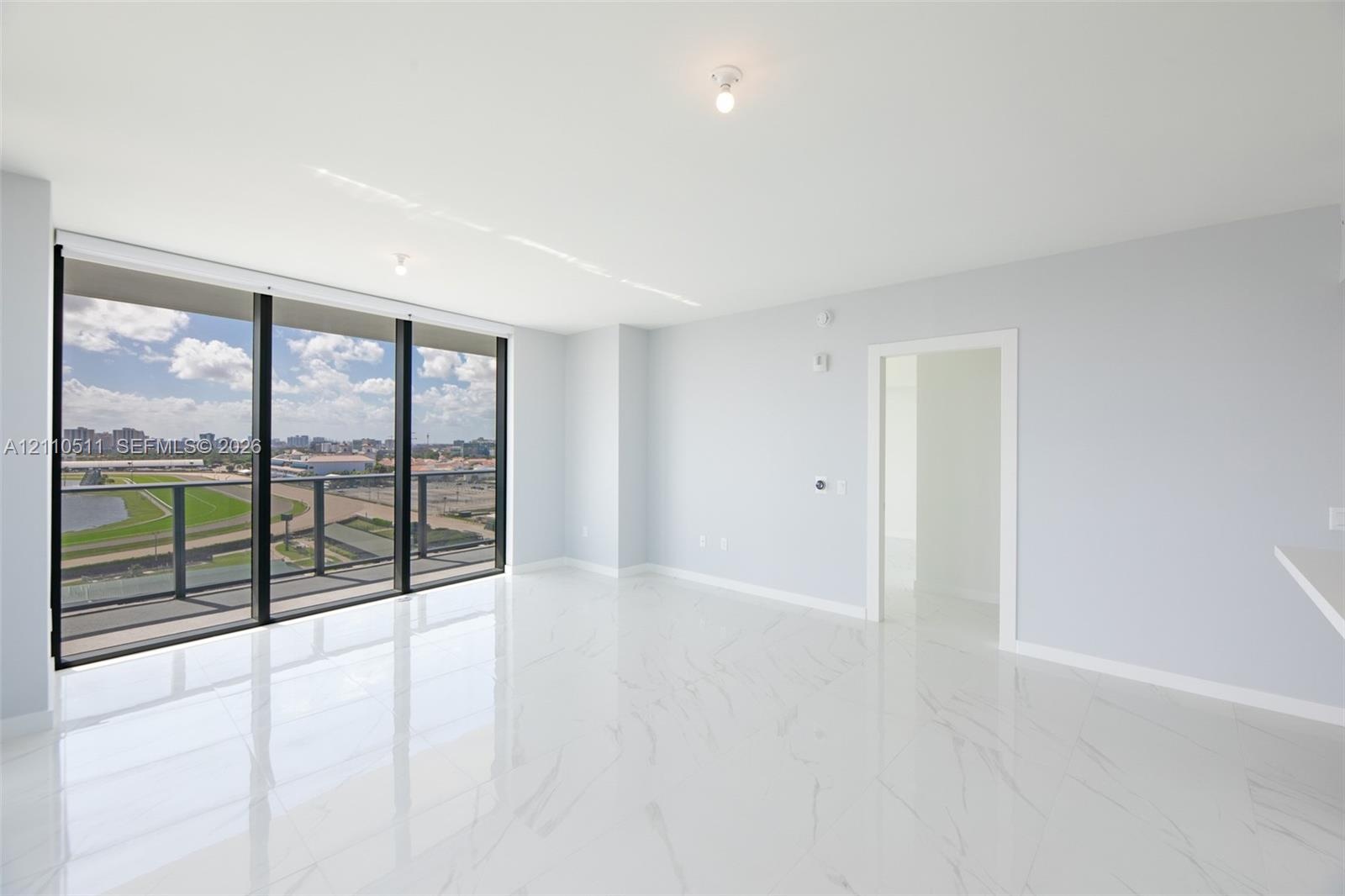 Open-concept interior featuring floor-to-ceiling glass windows, a private balcony with metal railing, and polished stone-finish tile flooring