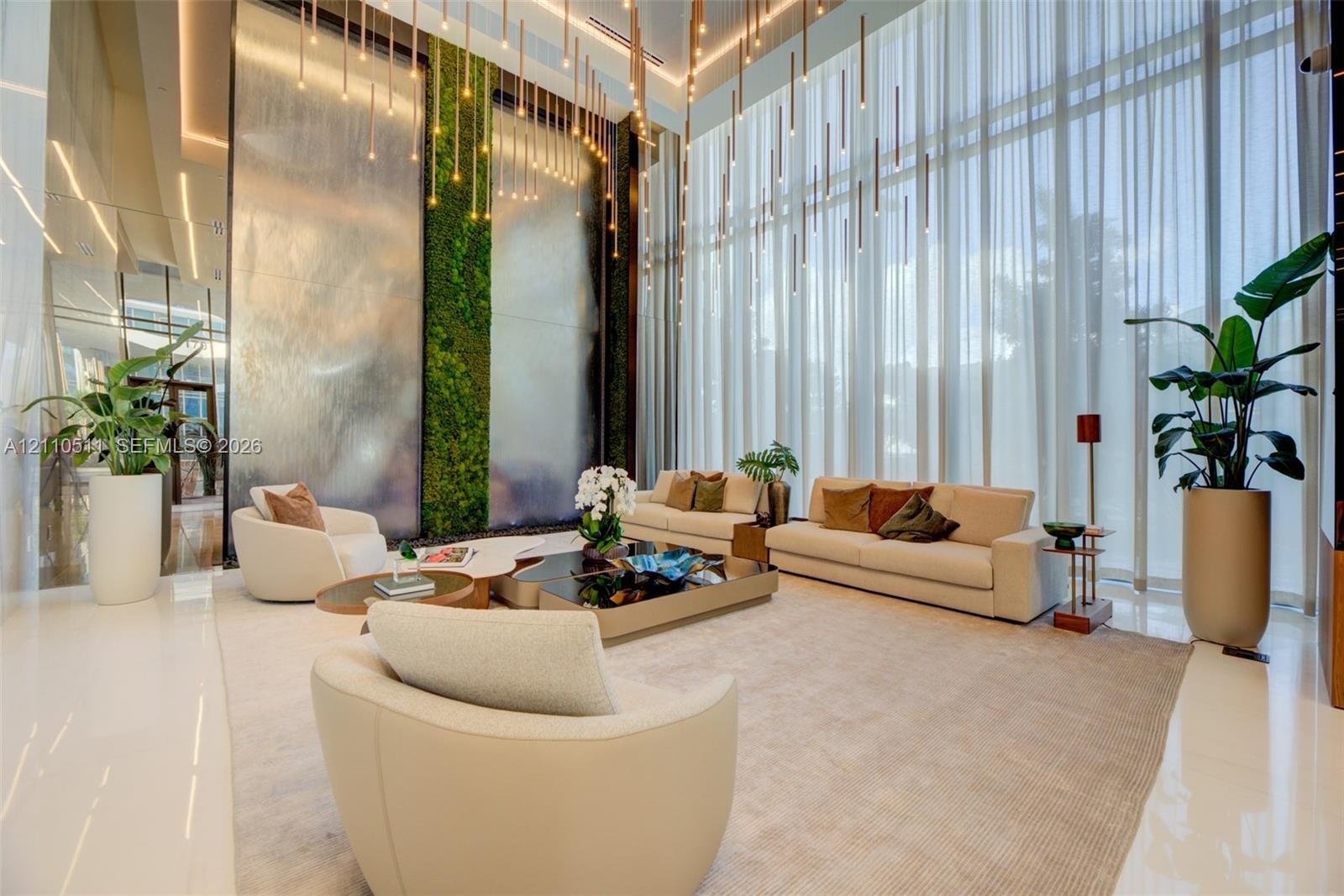 Double-height ceilings featuring floor-to-ceiling sheer drapery, a prominent indoor vertical living wall, a multi-panel decorative metal water feature