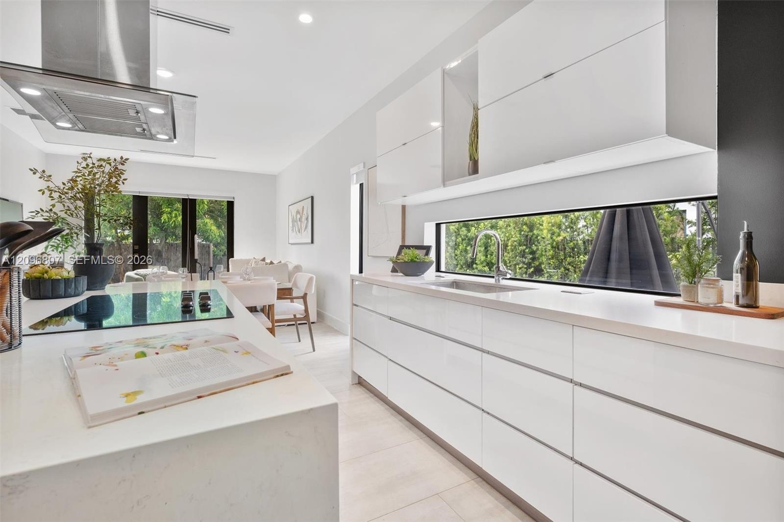 Contemporary kitchen featuring flat-panel high-gloss cabinetry, stone-surface countertops, a full-width horizontal backsplash window, a stainless stee