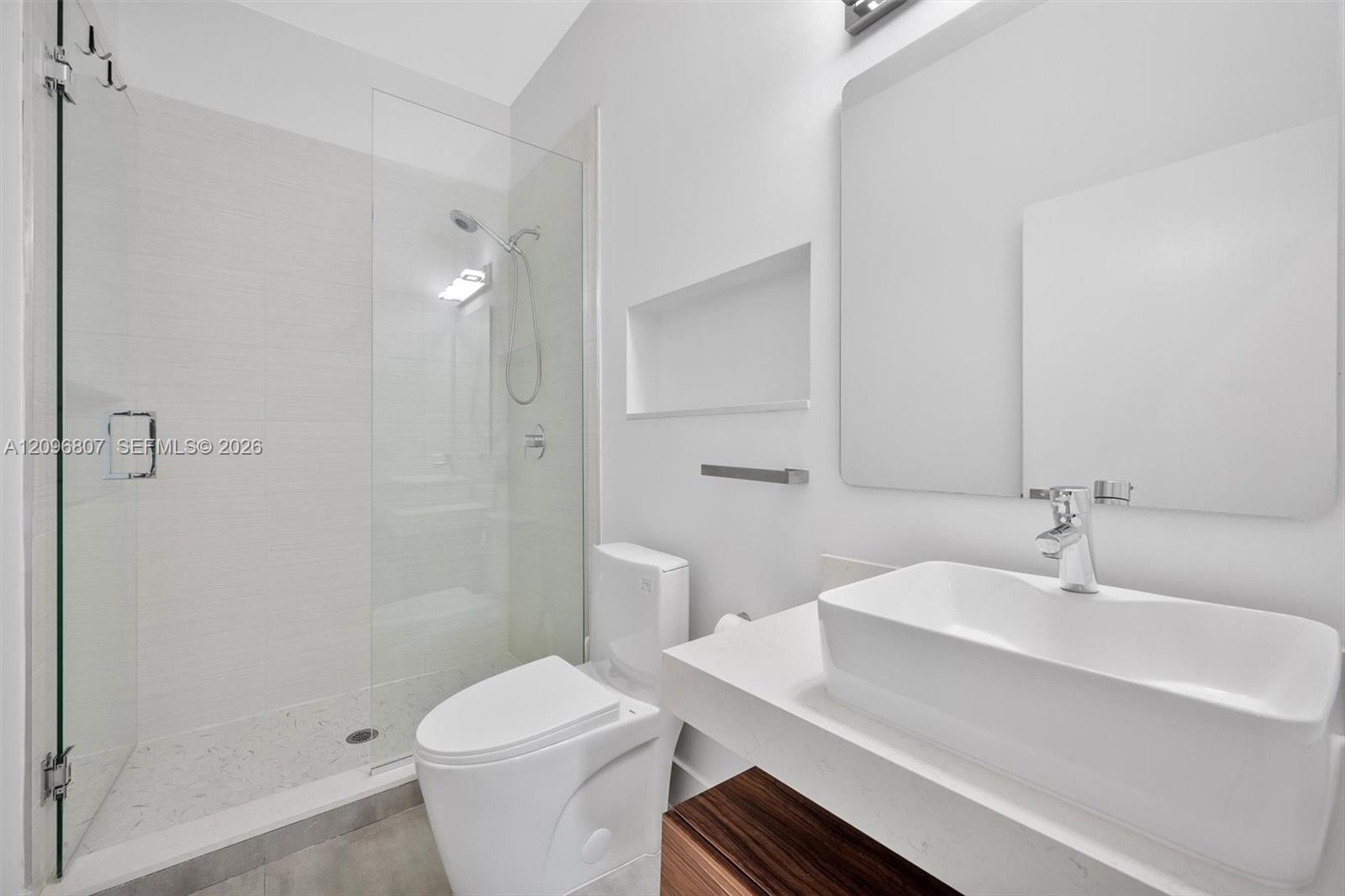Bathroom featuring a vessel sink with a white stone-composite countertop, wood-finish vanity cabinet, walk-in shower with a glass enclosure and built-