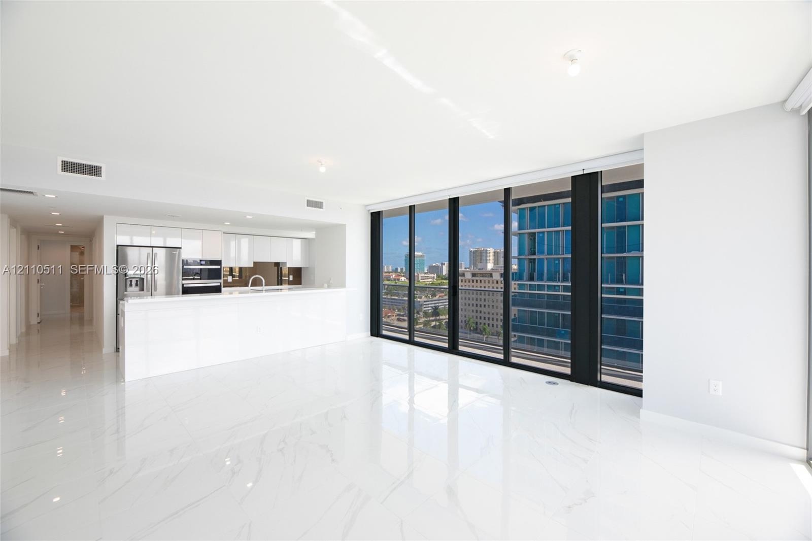 Open-concept living space featuring high-gloss tile flooring, floor-to-ceiling glass windows, and a minimalist kitchen equipped with white cabinetry a