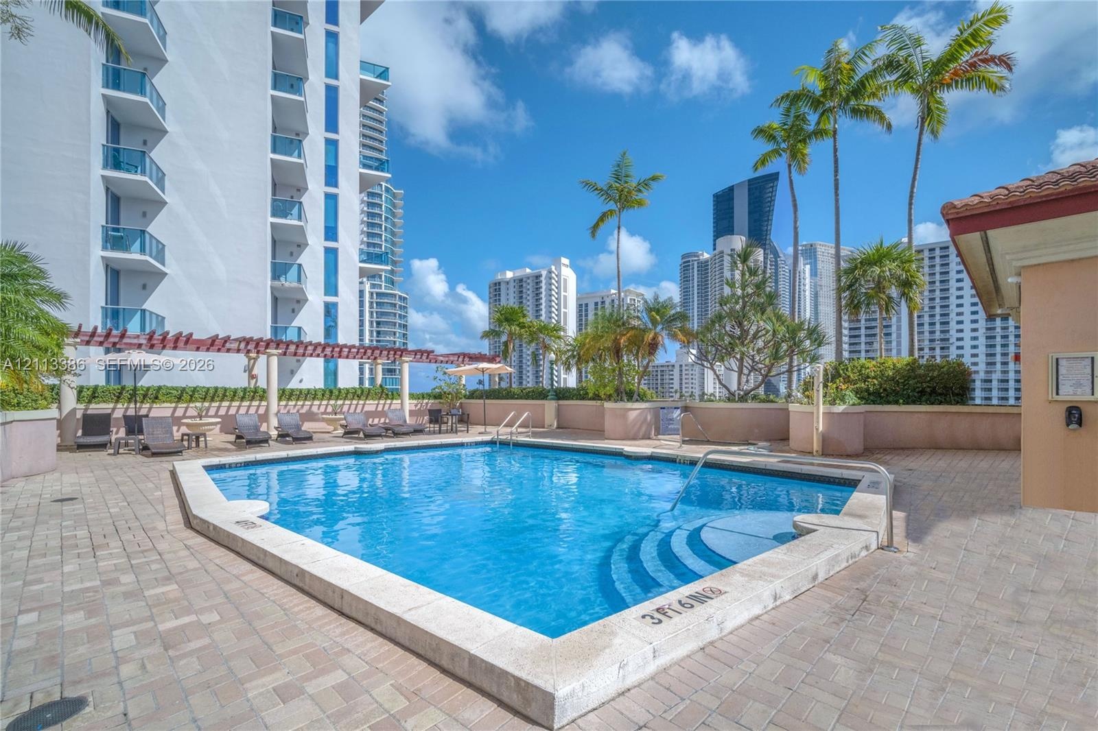 Swimming pool featuring a stone-paver deck, pergola-style covering, and palm tree landscaping
