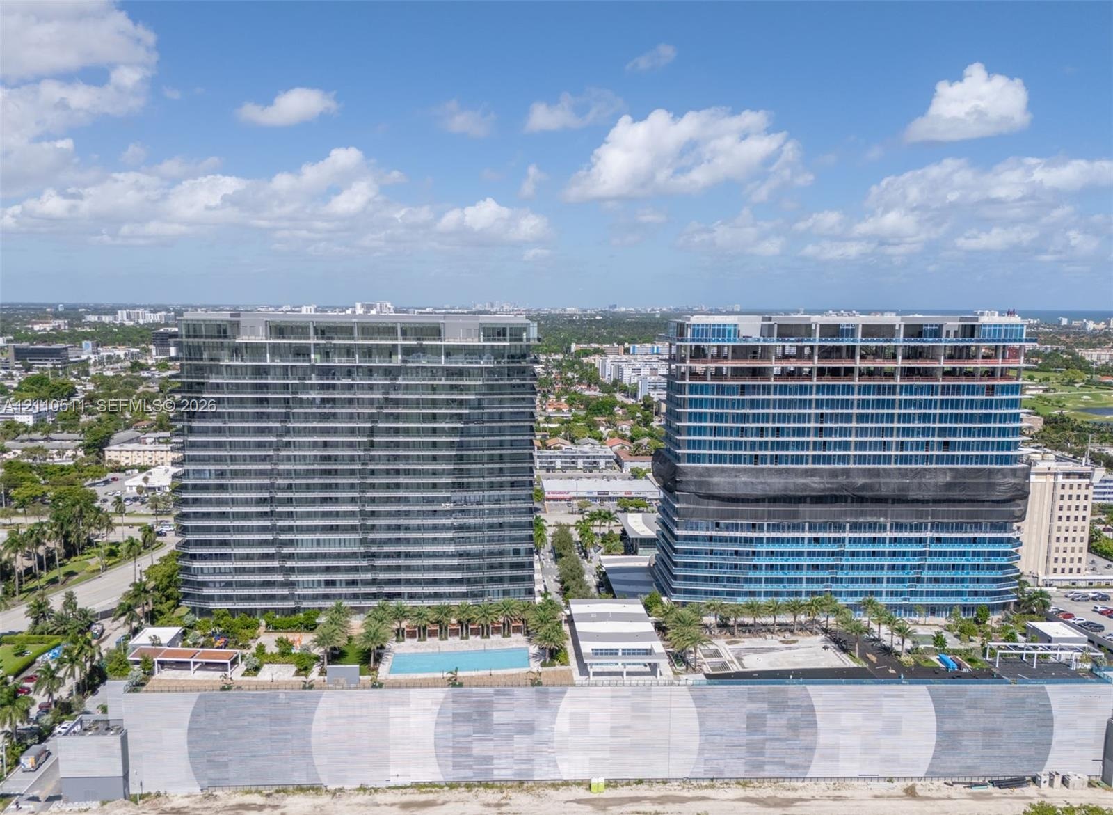 High-rise residential towers featuring expansive glass curtain wall facades, integrated swimming pool, landscaped outdoor ground-level area, and concr