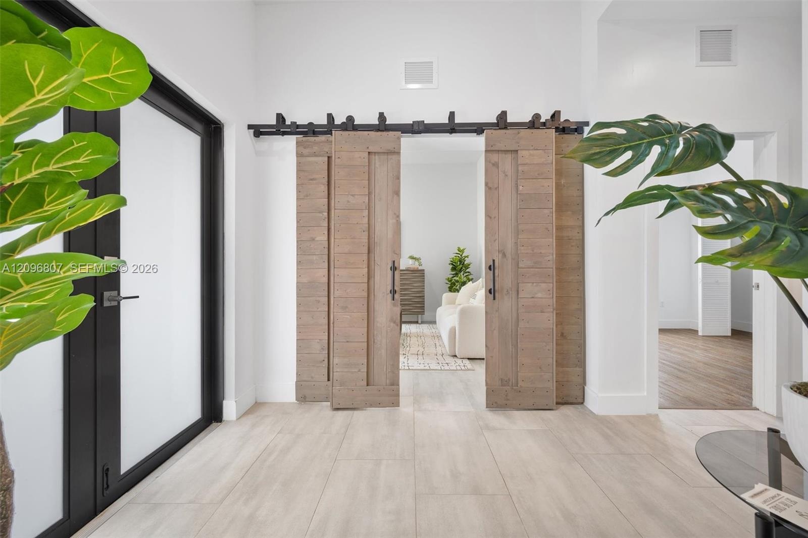 Double sliding barn doors with a matte black metal track system, wood-finish flooring, and black-framed glass entry door
