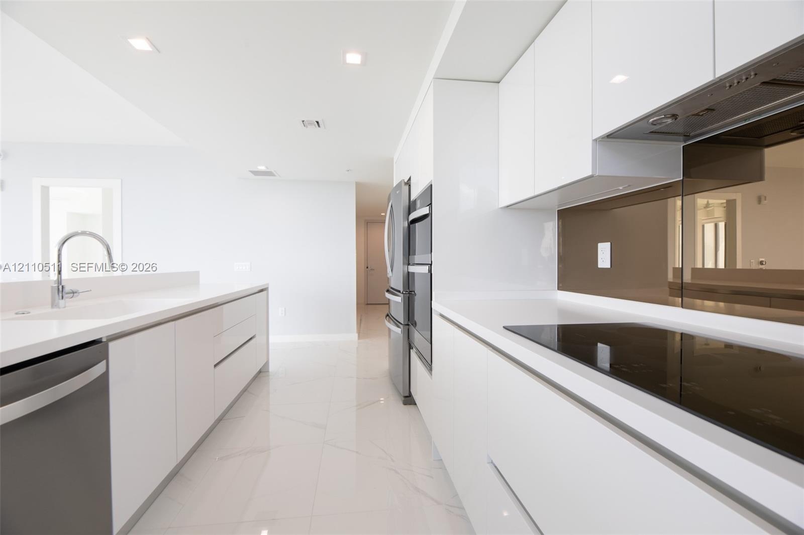 Modern kitchen featuring high-gloss white cabinetry, white stone countertops, integrated stainless steel appliances, a tinted glass backsplash, and po