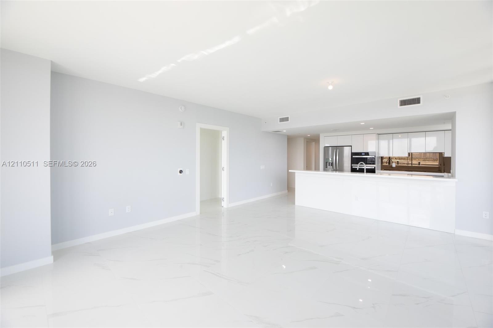 Open-concept interior featuring large-format tile flooring, white gloss cabinetry, a peninsula with a waterfall-edge countertop, and stainless steel b