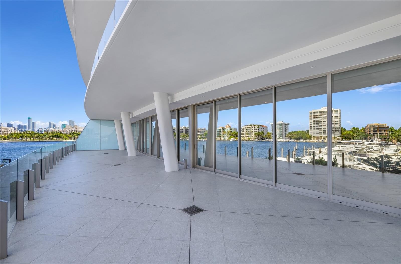 Expansive wraparound balcony featuring large-format tile flooring, a glass railing system, structural architectural pillars, and floor-to-ceiling glas