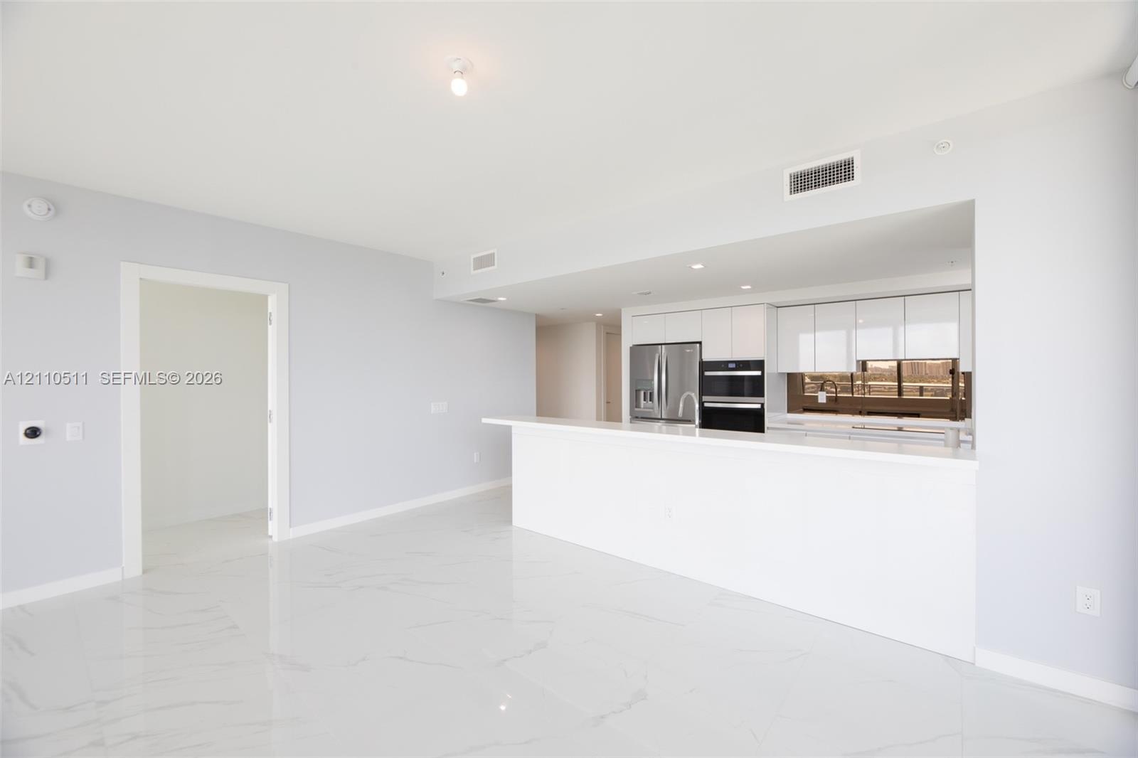 Open-concept area featuring white tile flooring with veining, white flat-panel cabinetry, a stone-surface peninsula, stainless steel appliances, and i