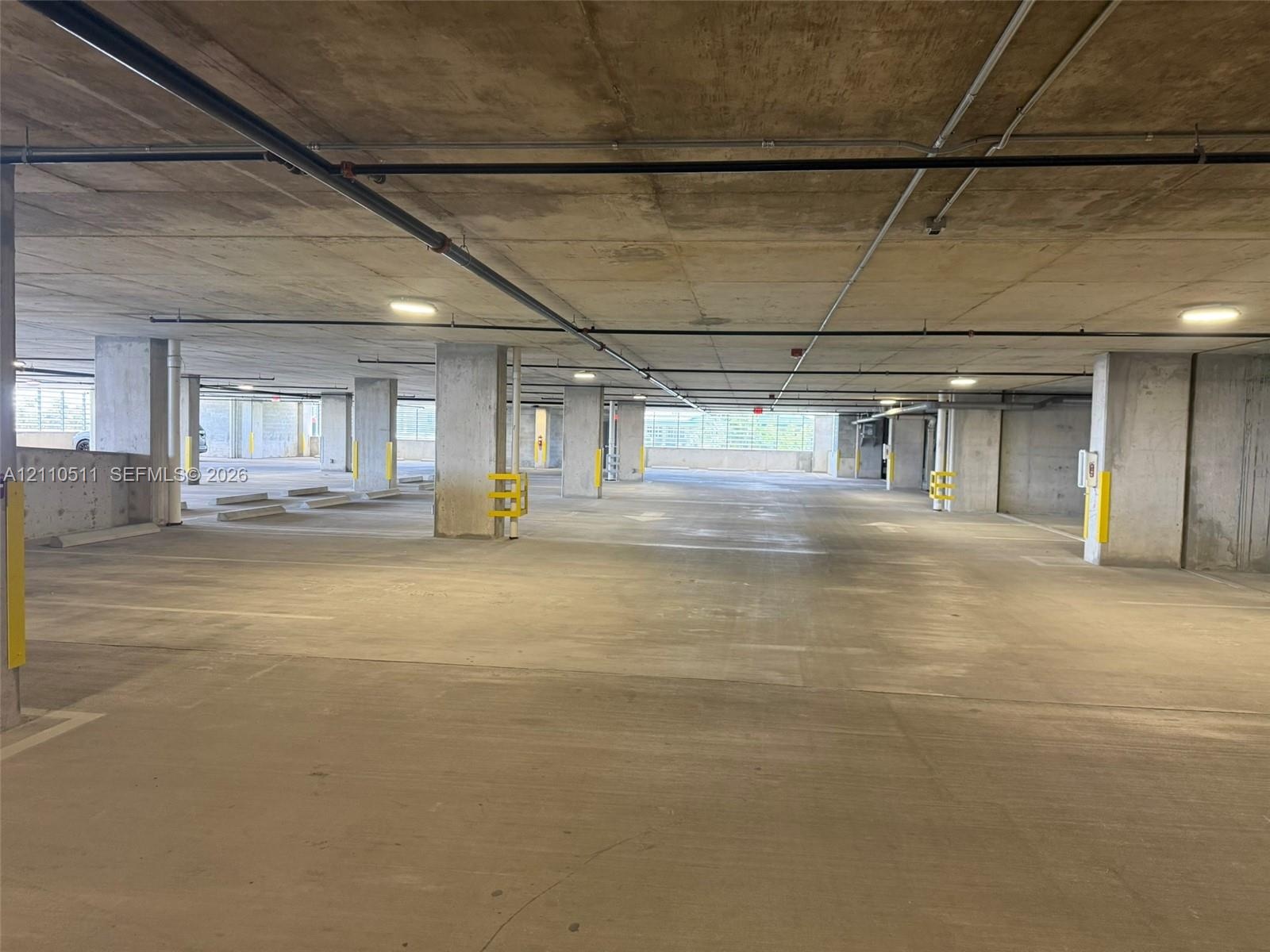 Covered parking garage featuring reinforced concrete structural columns, overhead flush-mount lighting, and concrete flooring