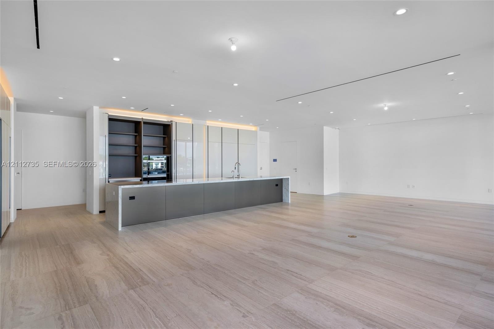Minimalist kitchen featuring an expansive island with metallic cabinetry, light-toned stone countertops, built-in shelving, integrated lighting, and w