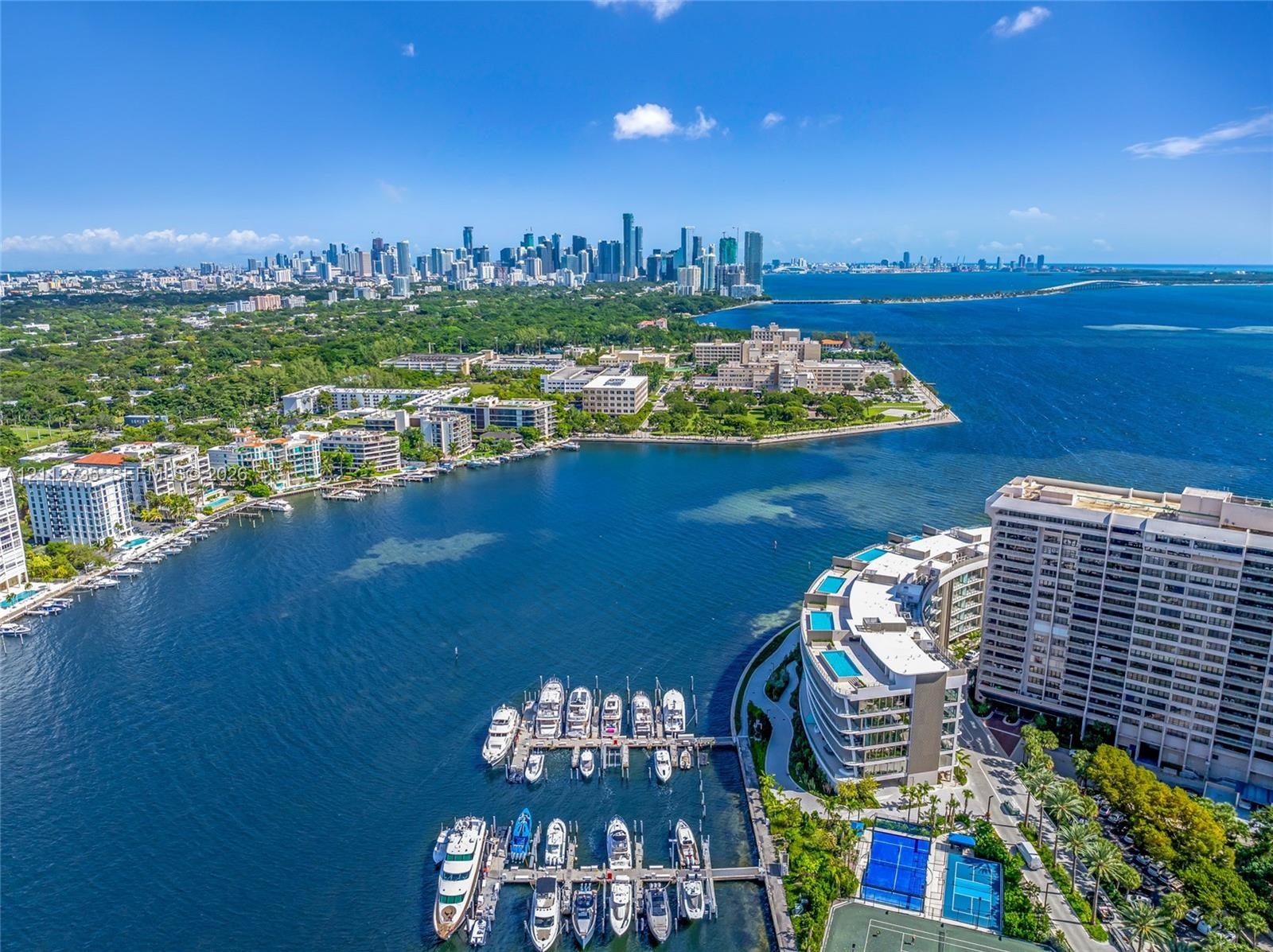 Aerial perspective of waterfront property featuring a private boat dock, marina slip access, tennis courts, and landscaped grounds