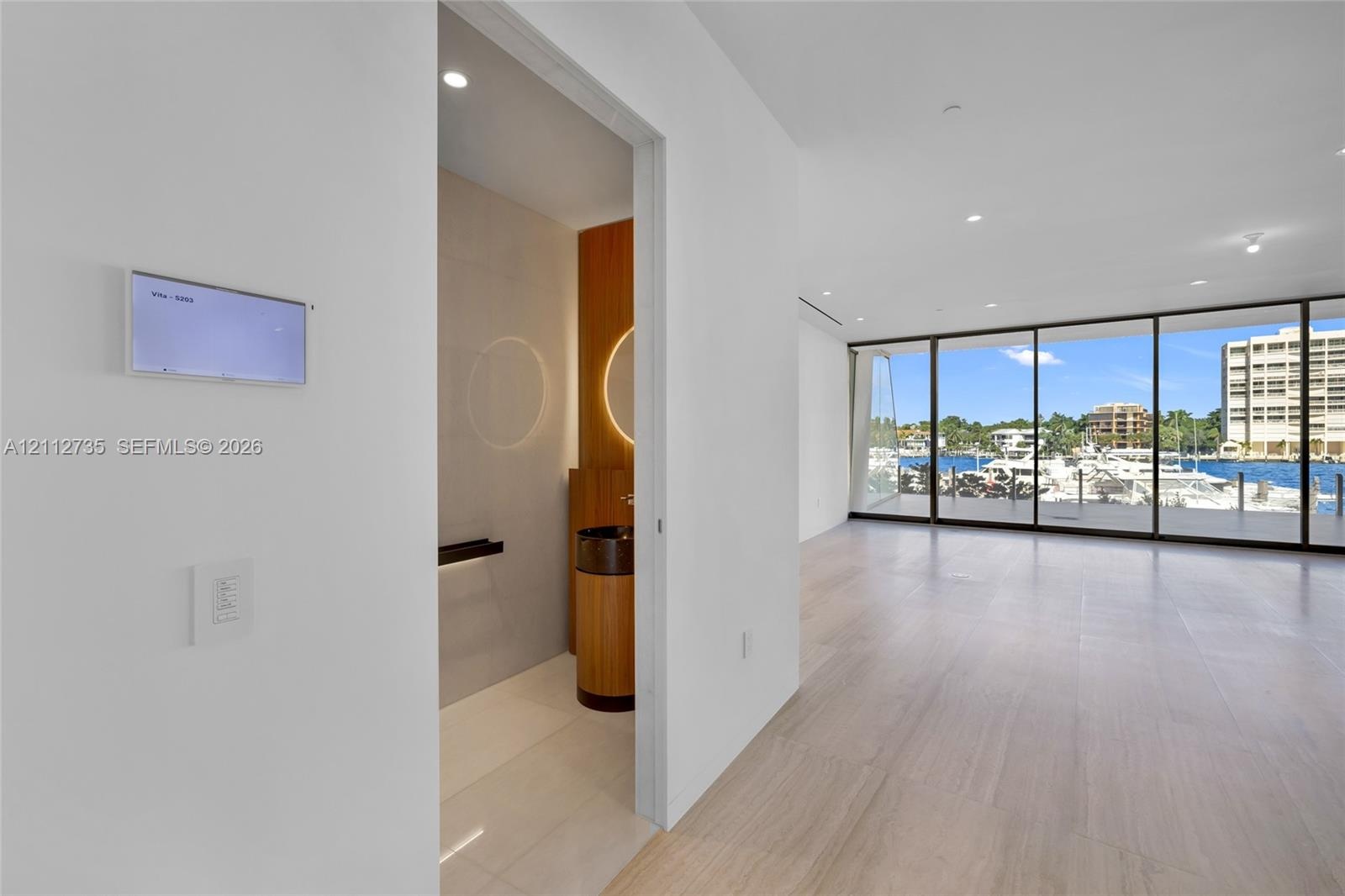 Floor-to-ceiling glass wall, wood-finish flooring, recessed lighting, and wall-mounted smart home control panel, featuring a powder room with cylindri