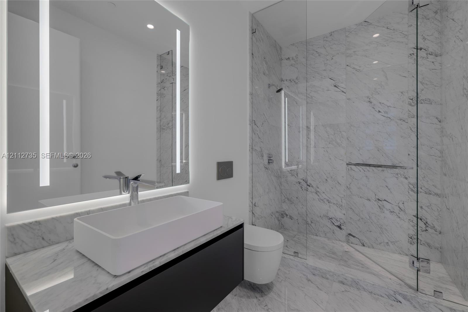 Floating vanity with integrated countertop, rectangular vessel sink, wall-to-wall mirror with vertical integrated lighting, glass-enclosed shower, and