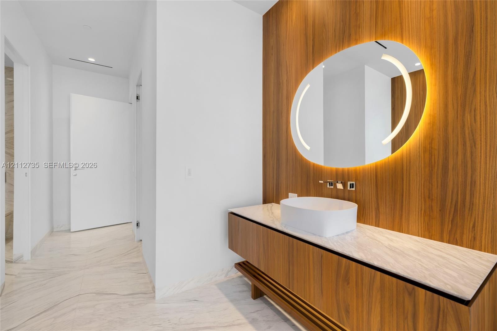 Floating wood-finish vanity with a stone countertop, white vessel sink, wall-mounted faucet, and custom wood-paneled wall featuring an integrated circ