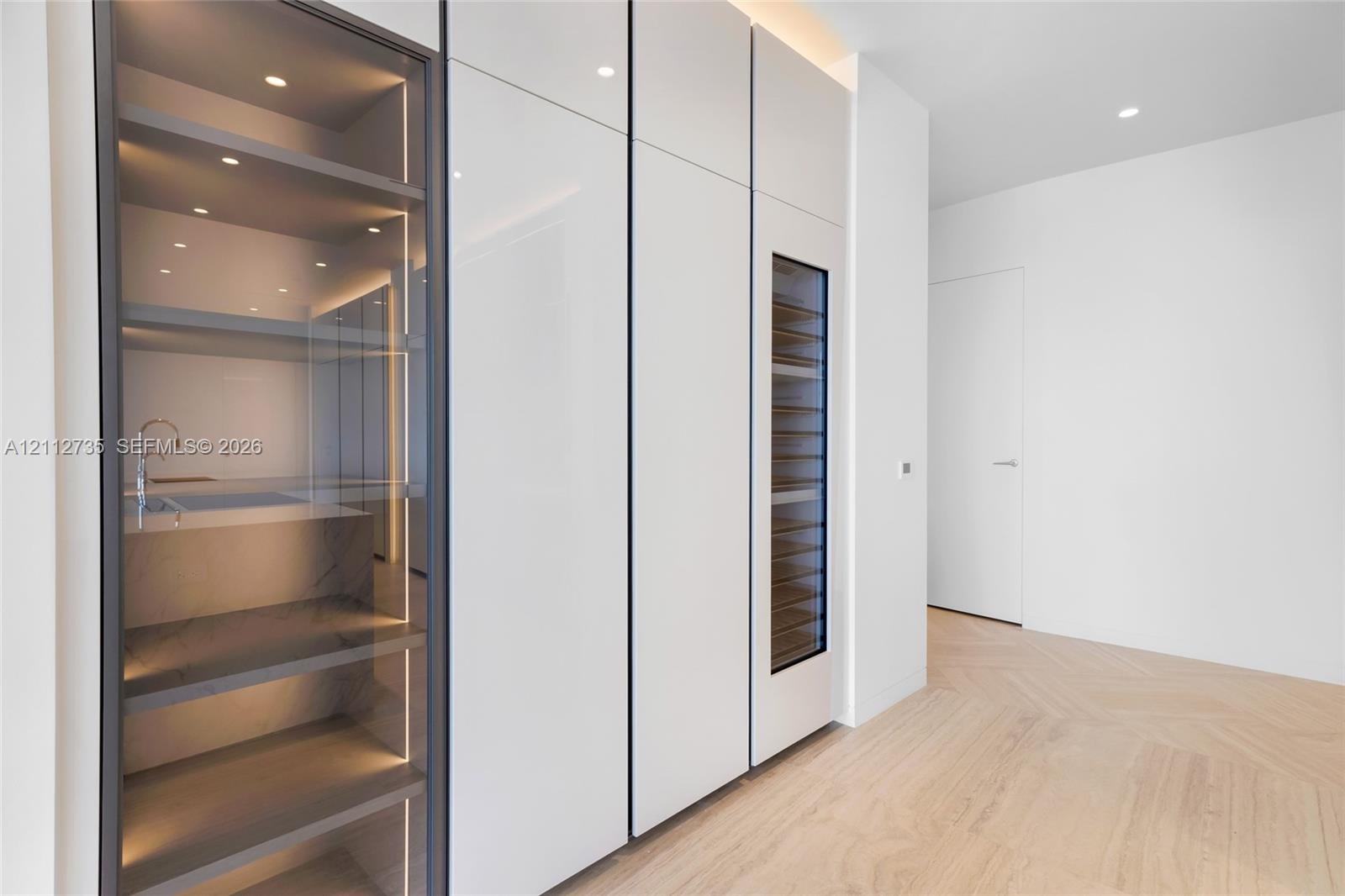 Custom millwork featuring floor-to-ceiling high-gloss cabinetry, integrated wine refrigeration, glass-front display shelving with LED illumination, an