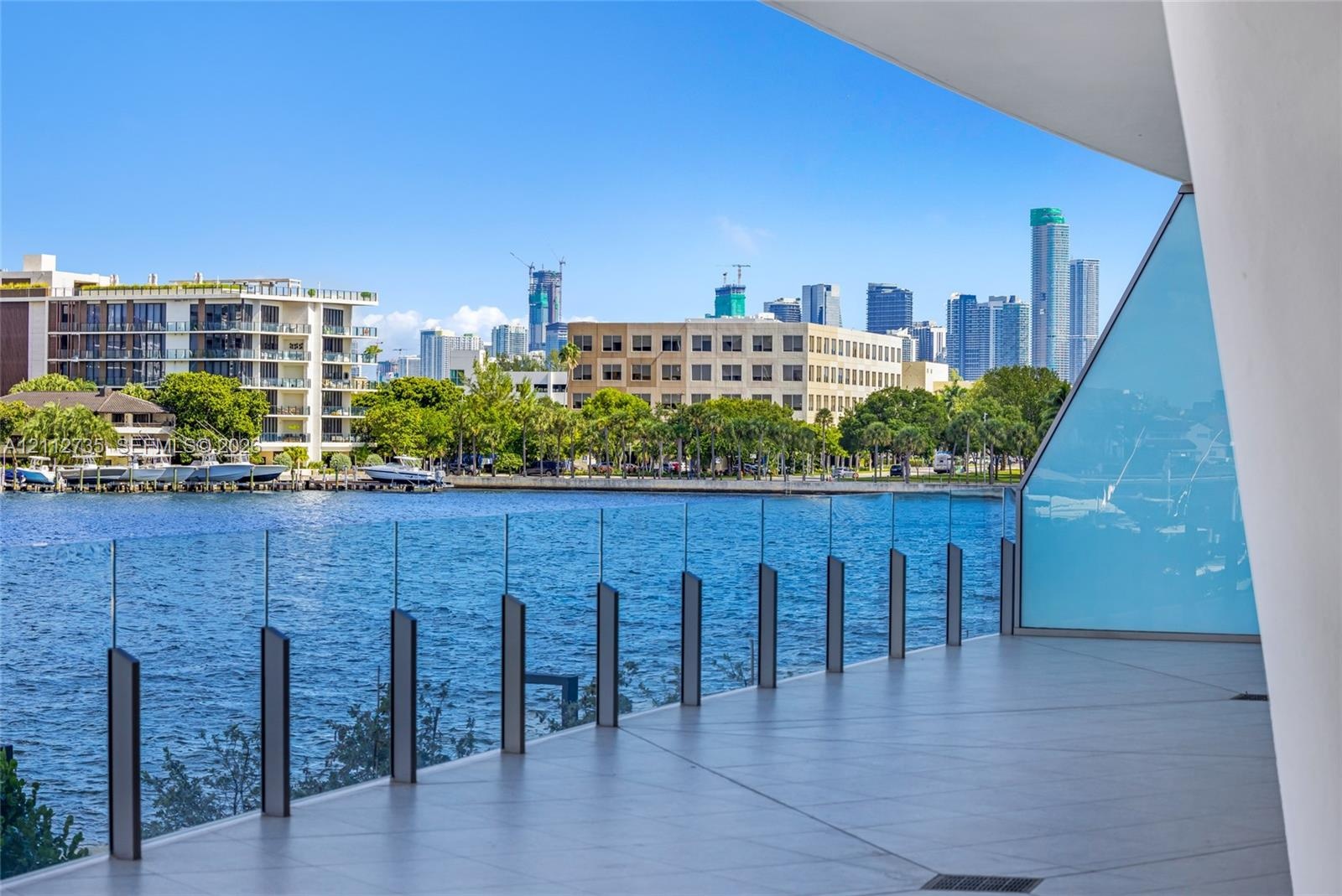 Covered balcony featuring large-format tile flooring and a transparent glass railing with vertical metal supports, overlooking a waterway