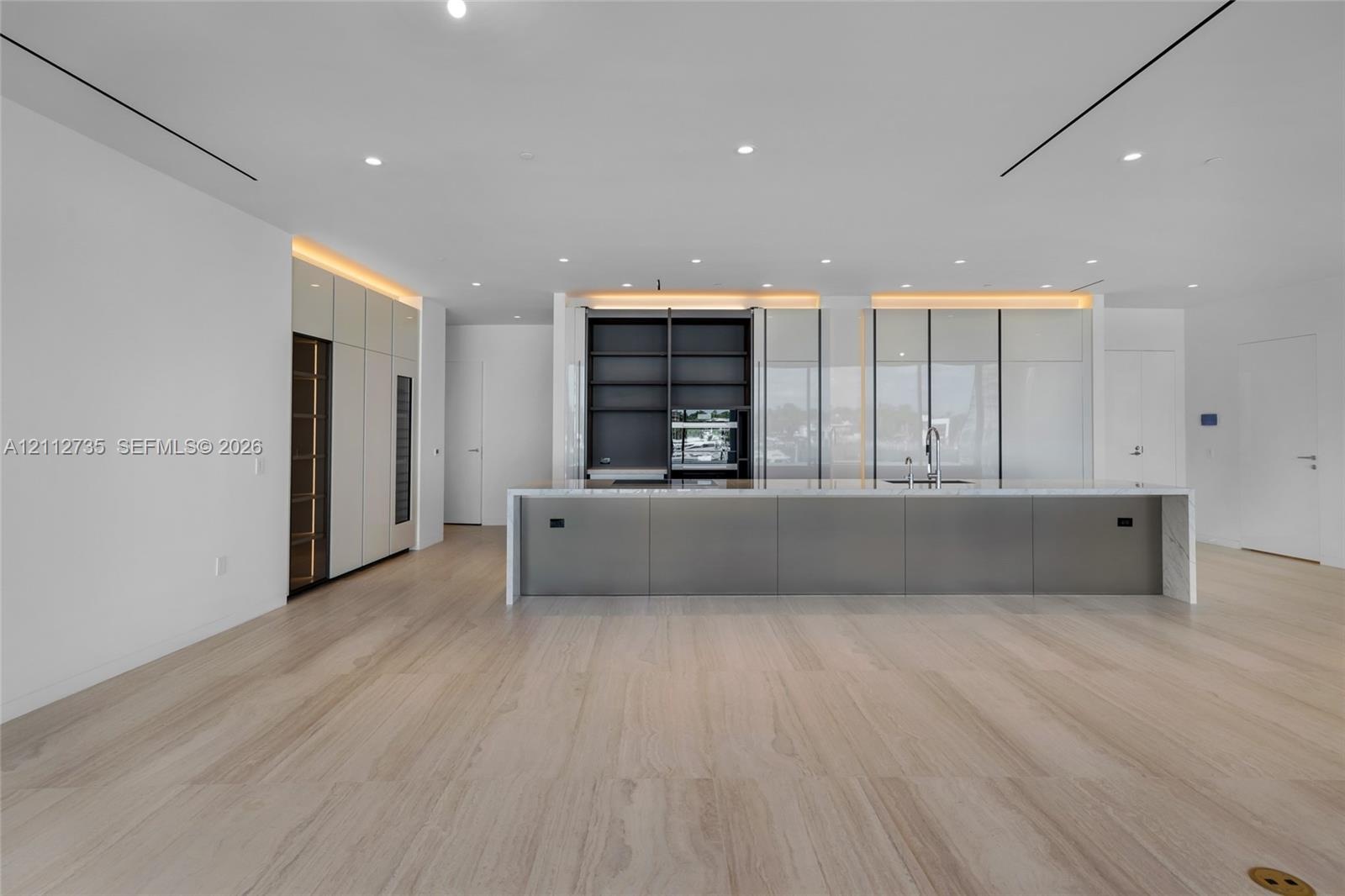Modern kitchen featuring floor-to-ceiling cabinetry, a sprawling central island with stone-finish countertops, built-in dual wall ovens, recessed line